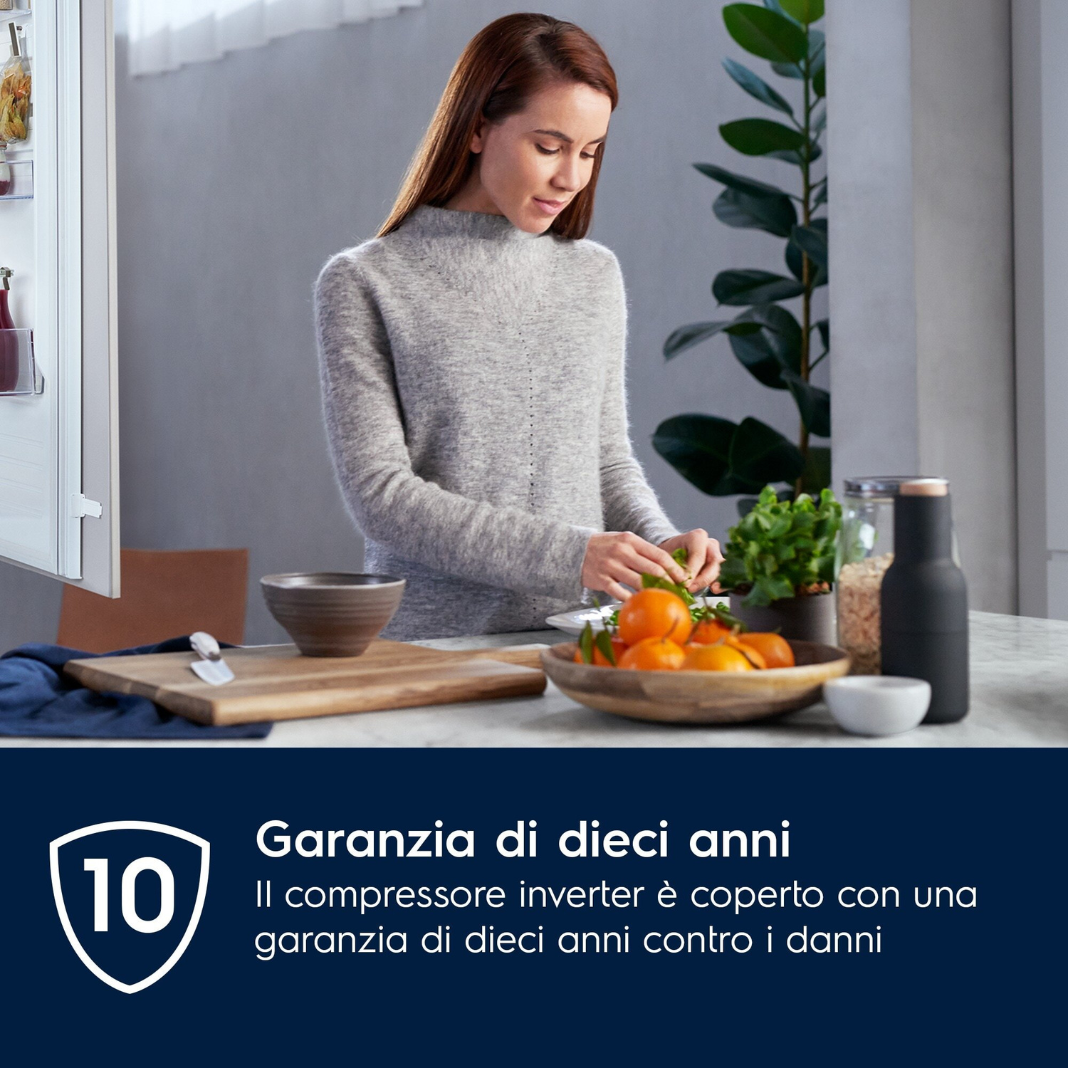 Donna in maglione grigio prepara cibo vicino a un frigorifero.