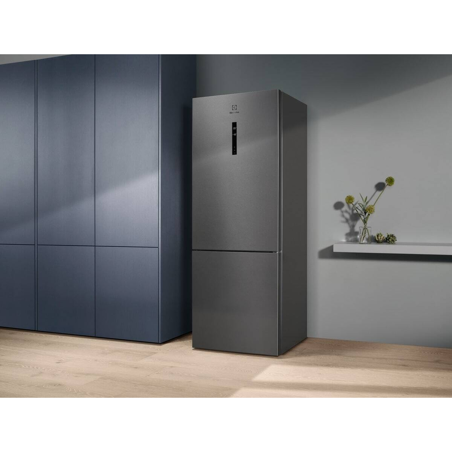 Un frigorifero grigio moderno accanto ad armadi blu scuro su pavimento in legno.