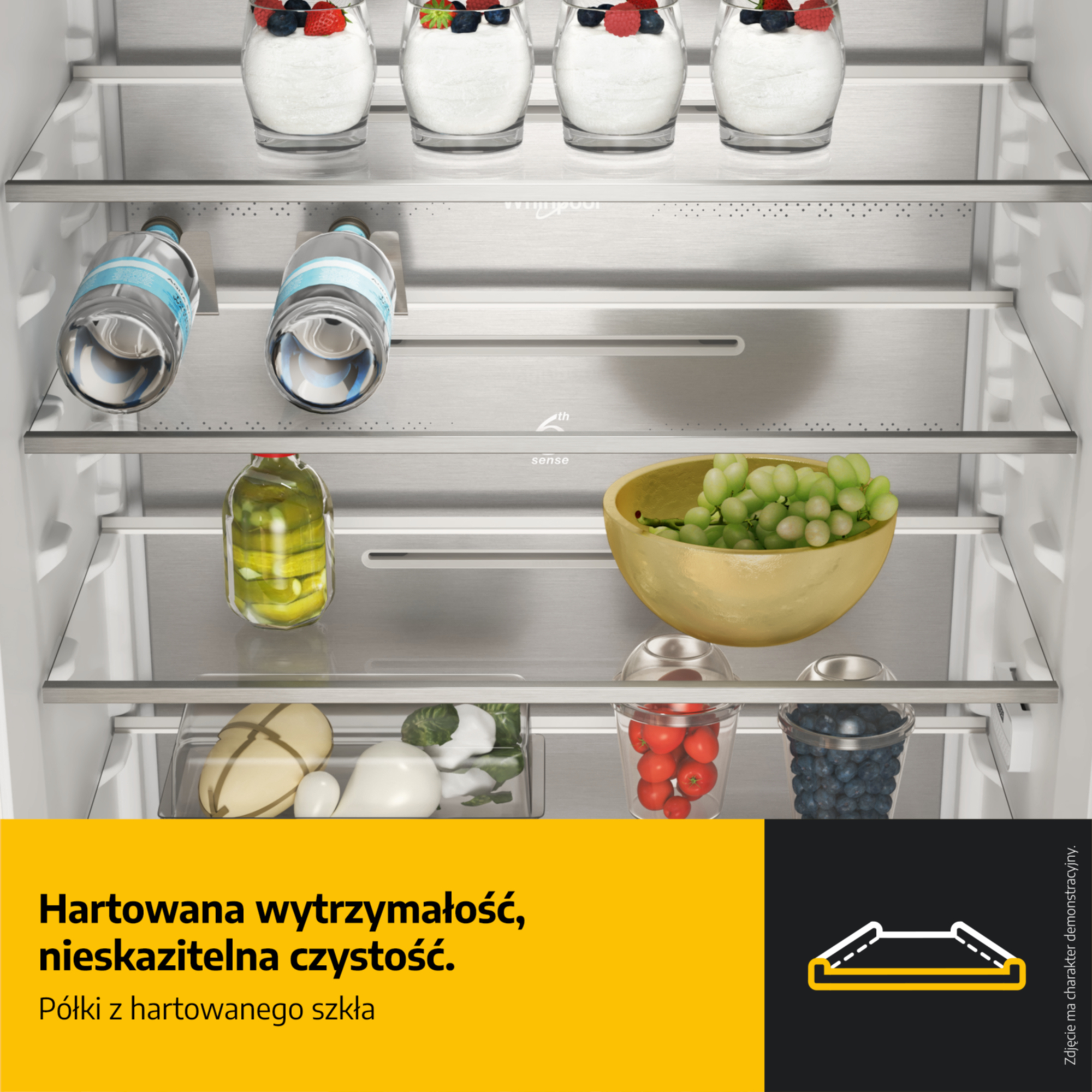 Lodówka z szklanymi półkami, zawierająca desery, butelki wody, ogórki, winogrona i jagody.