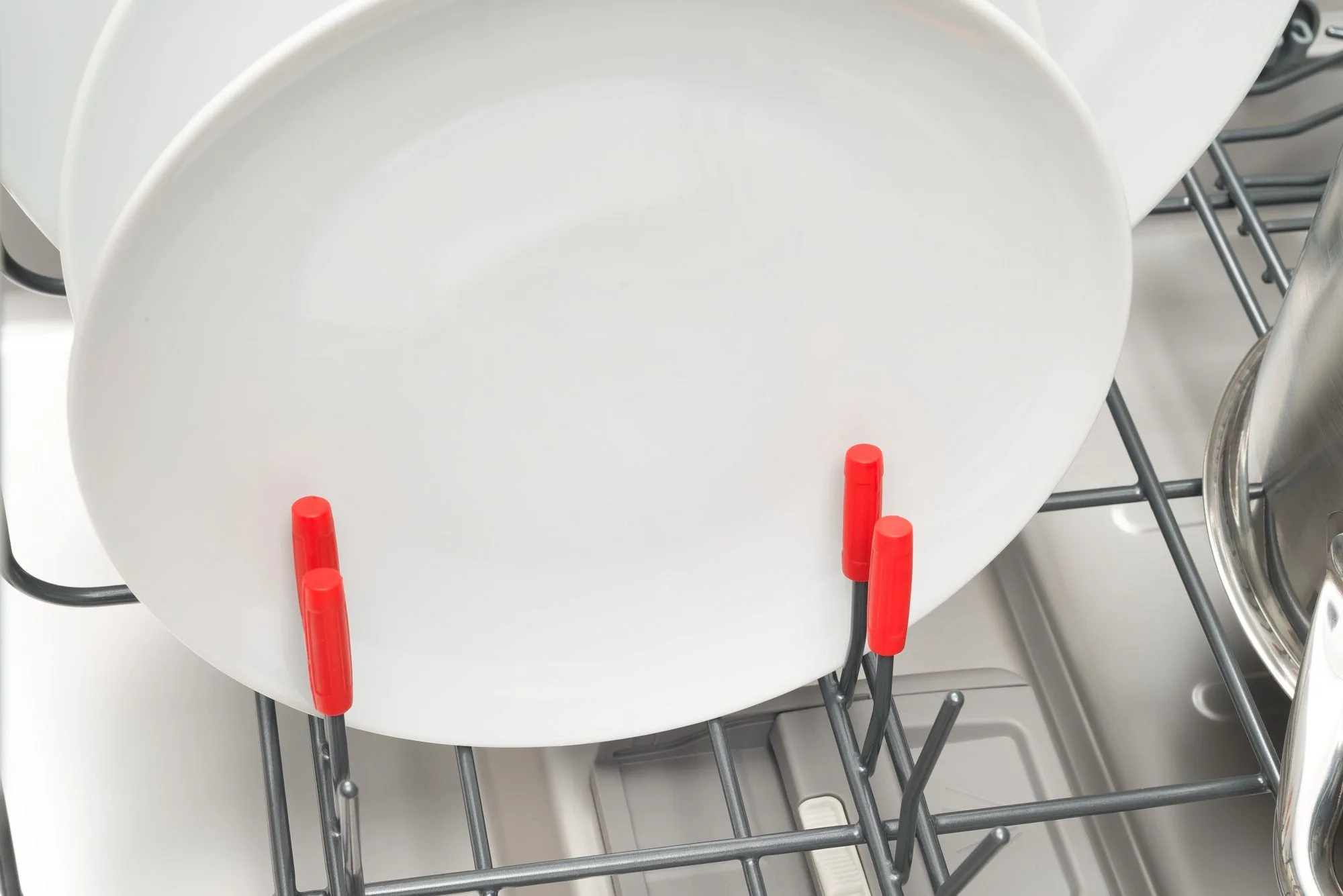 Białe talerze z czerwonymi uchwytami w zmywarce.
