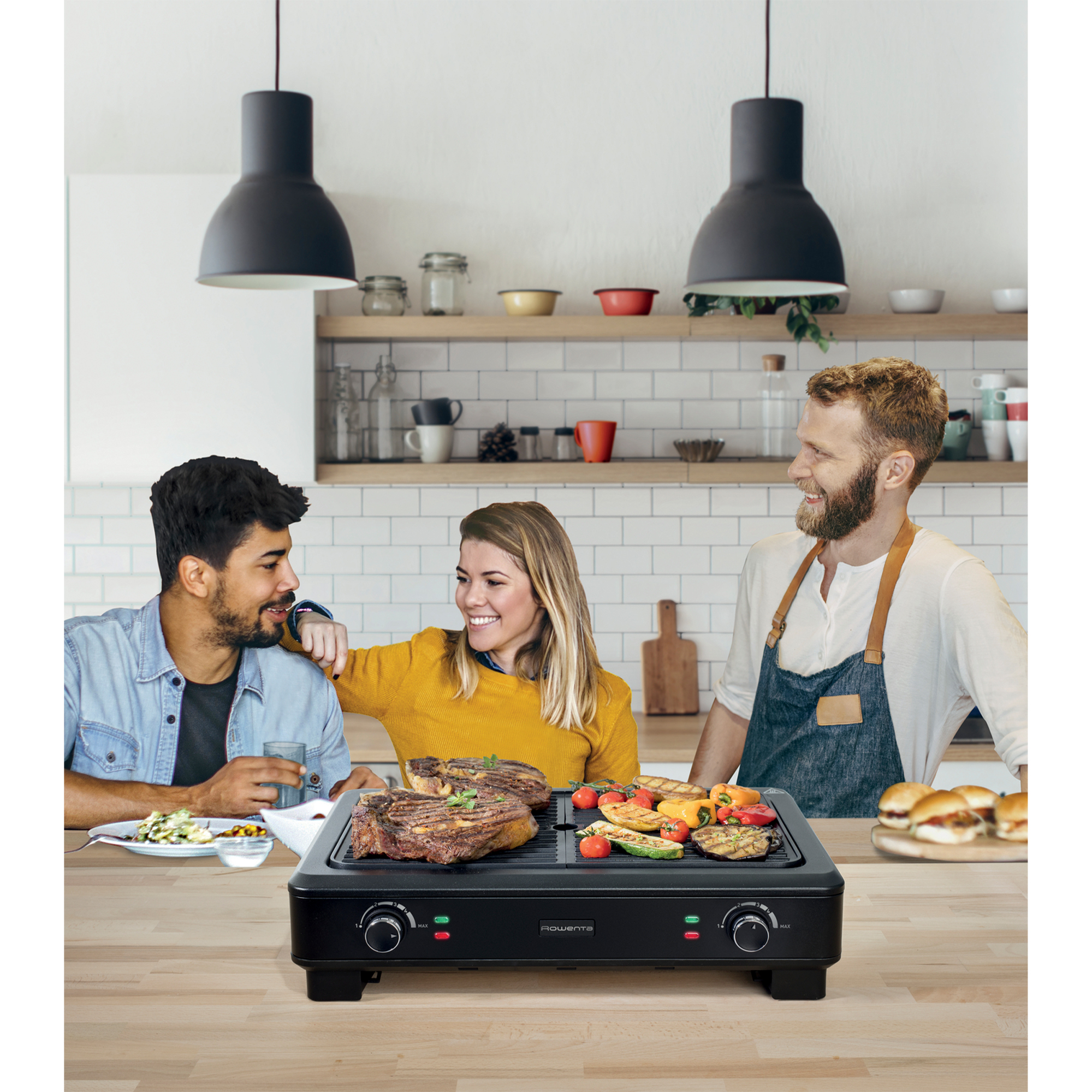 Tre persone gustano bistecche e verdure grigliate in una cucina moderna.