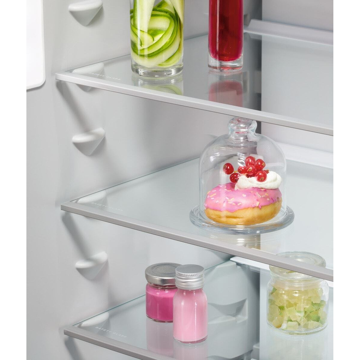 Una ciambella glassata rosa con bacche sotto una campana di vetro su uno scaffale.