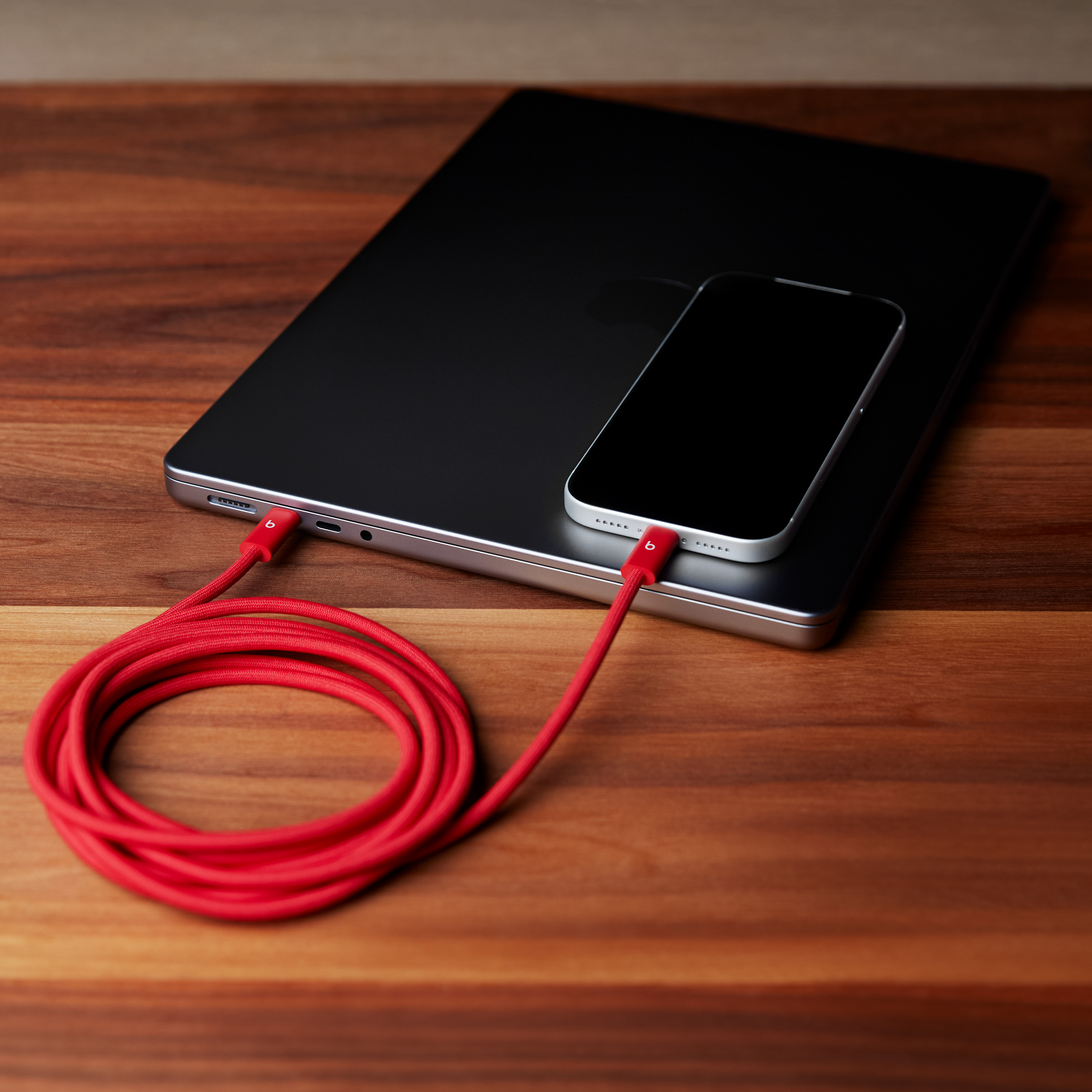 Ein rotes Kabel verbindet ein Handy mit einem Laptop auf einem Holztisch.