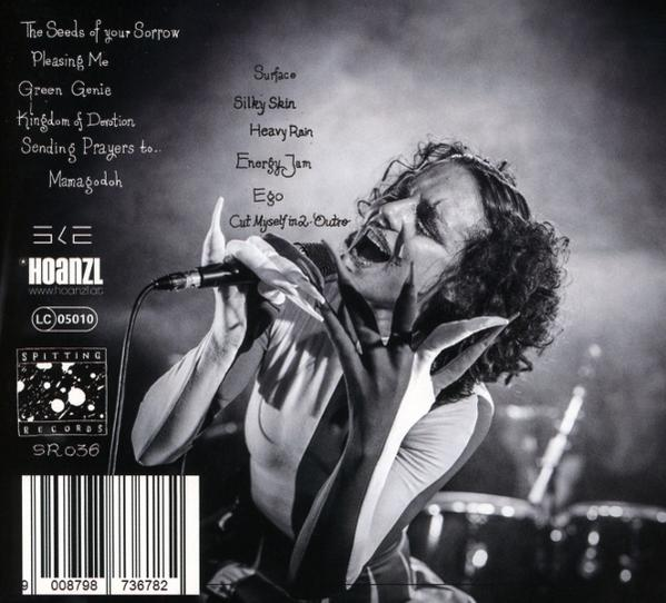 Eine Sängerin mit lockigem Haar singt in ein Mikrofon, Album-Trackliste im Hintergrund.