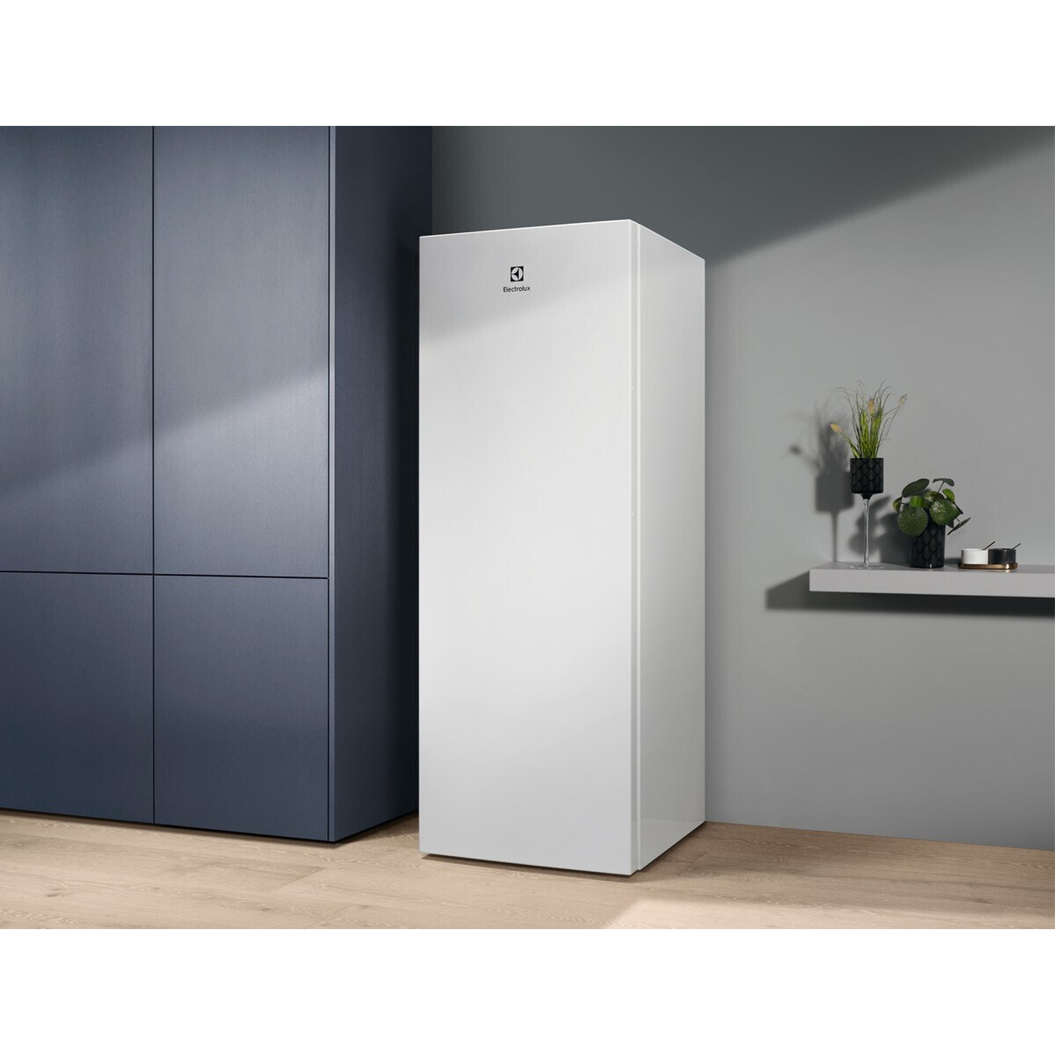Un congelatore bianco Electrolux accanto ad armadi grigio scuro su pavimento in legno.
