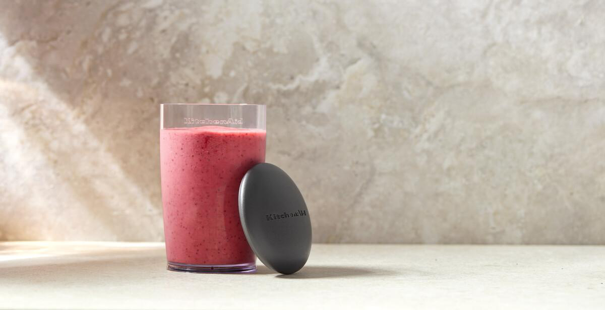 Ein Glas mit rotem Smoothie und ein grauer Deckel stehen auf einer Arbeitsplatte.