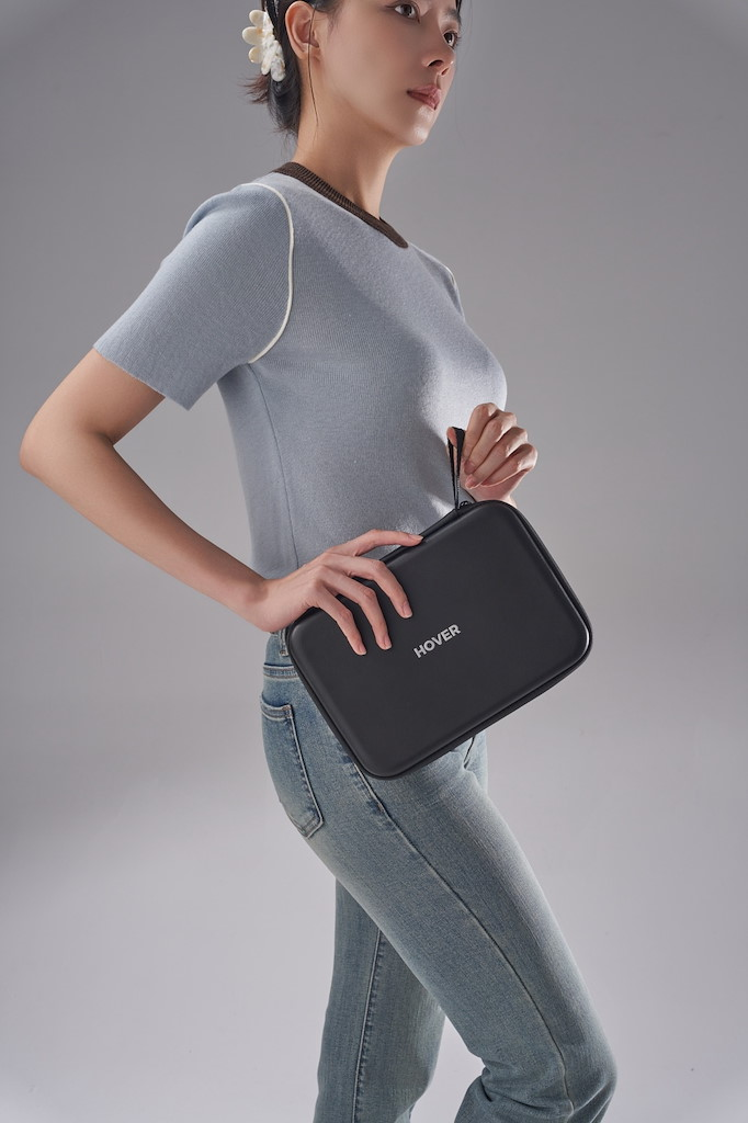 Eine Frau mit blauer Strickjacke und Jeans hält eine schwarze Tasche mit Aufschrift HOVER.