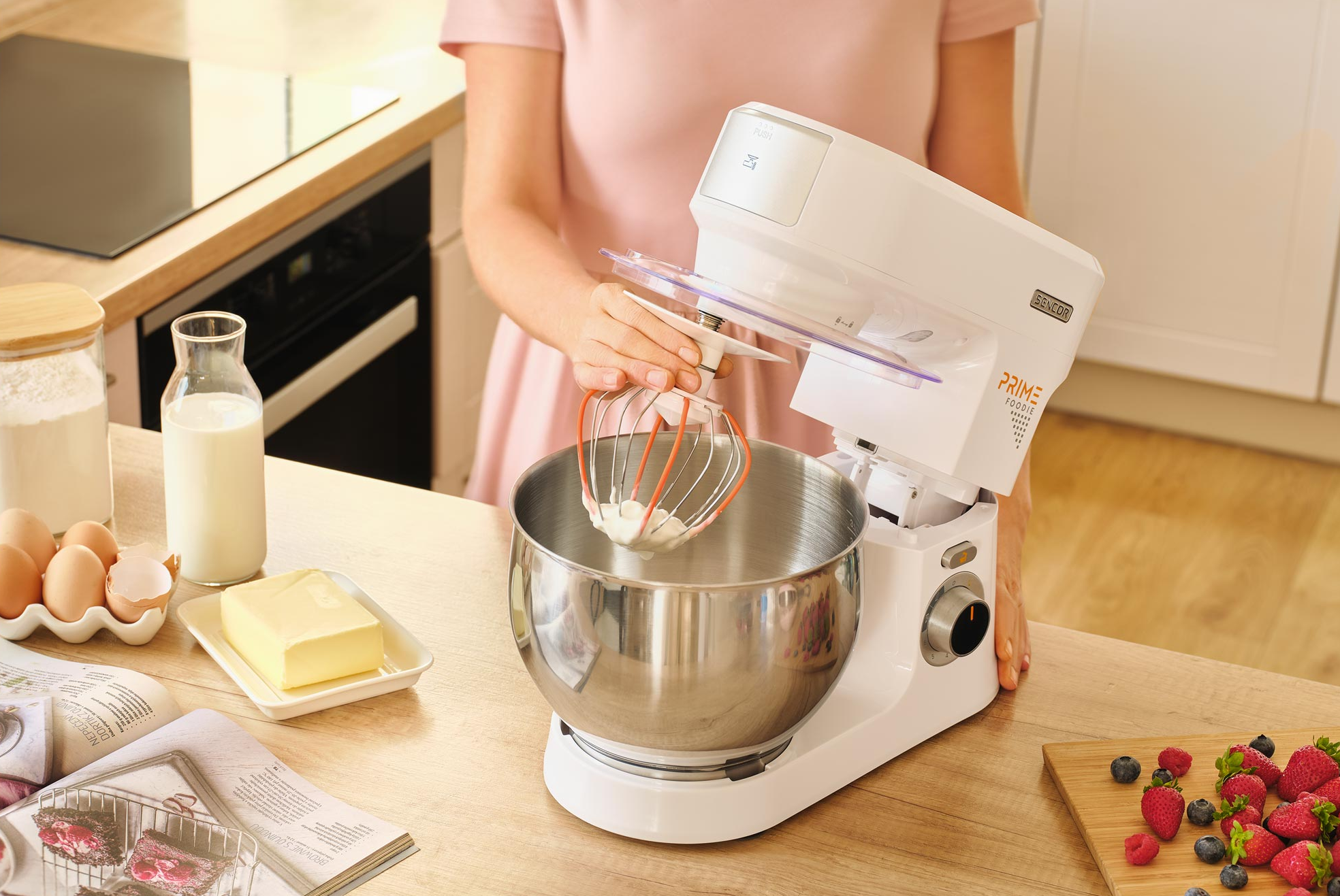 Fehér konyhai robotgép habverővel, tojásokkal, tejjel, vajjal és bogyókkal.