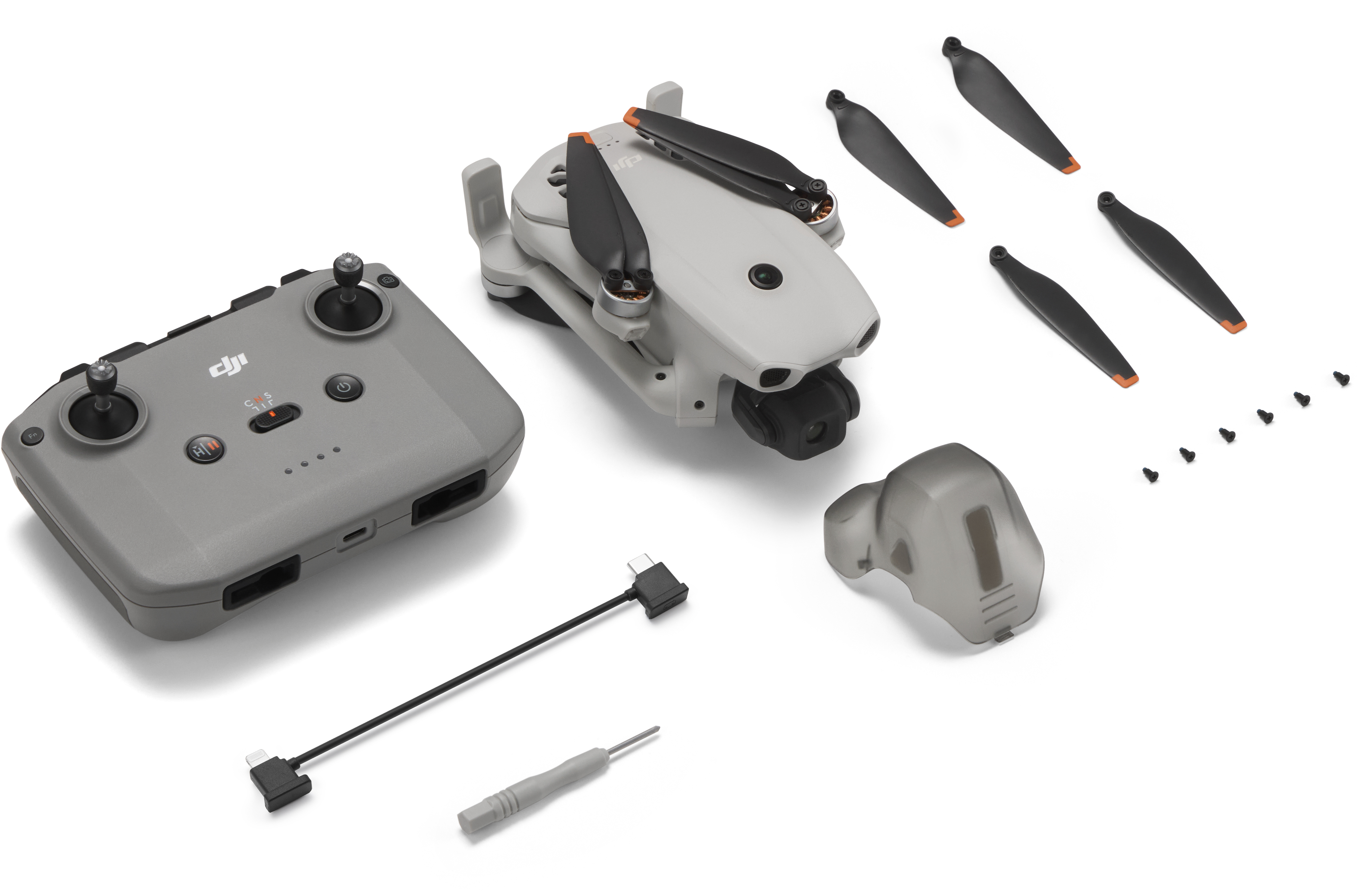 Drone grigio, controller, eliche, viti e cavo su sfondo bianco.