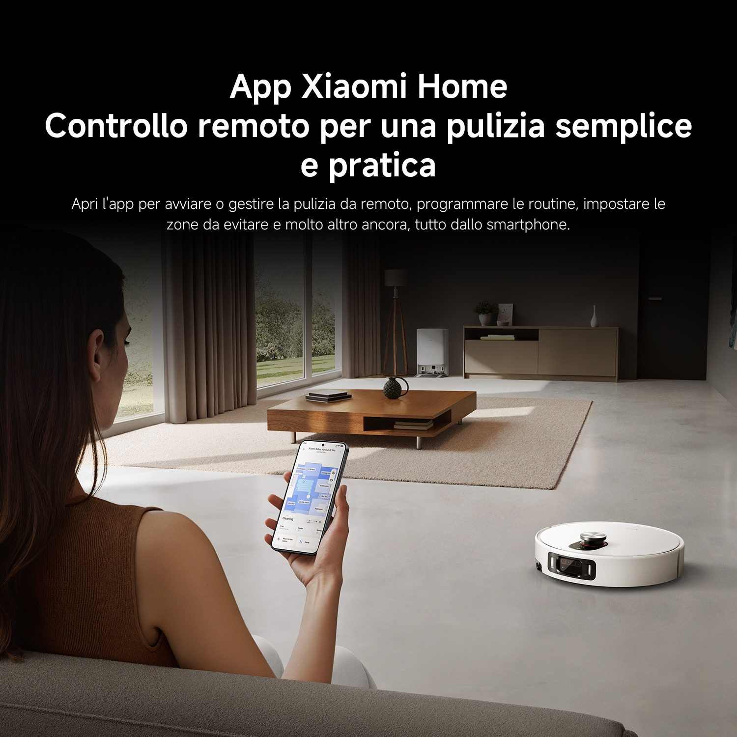 Una donna tiene uno smartphone con l'app Xiaomi Home, con un robot aspirapolvere sullo sfondo.