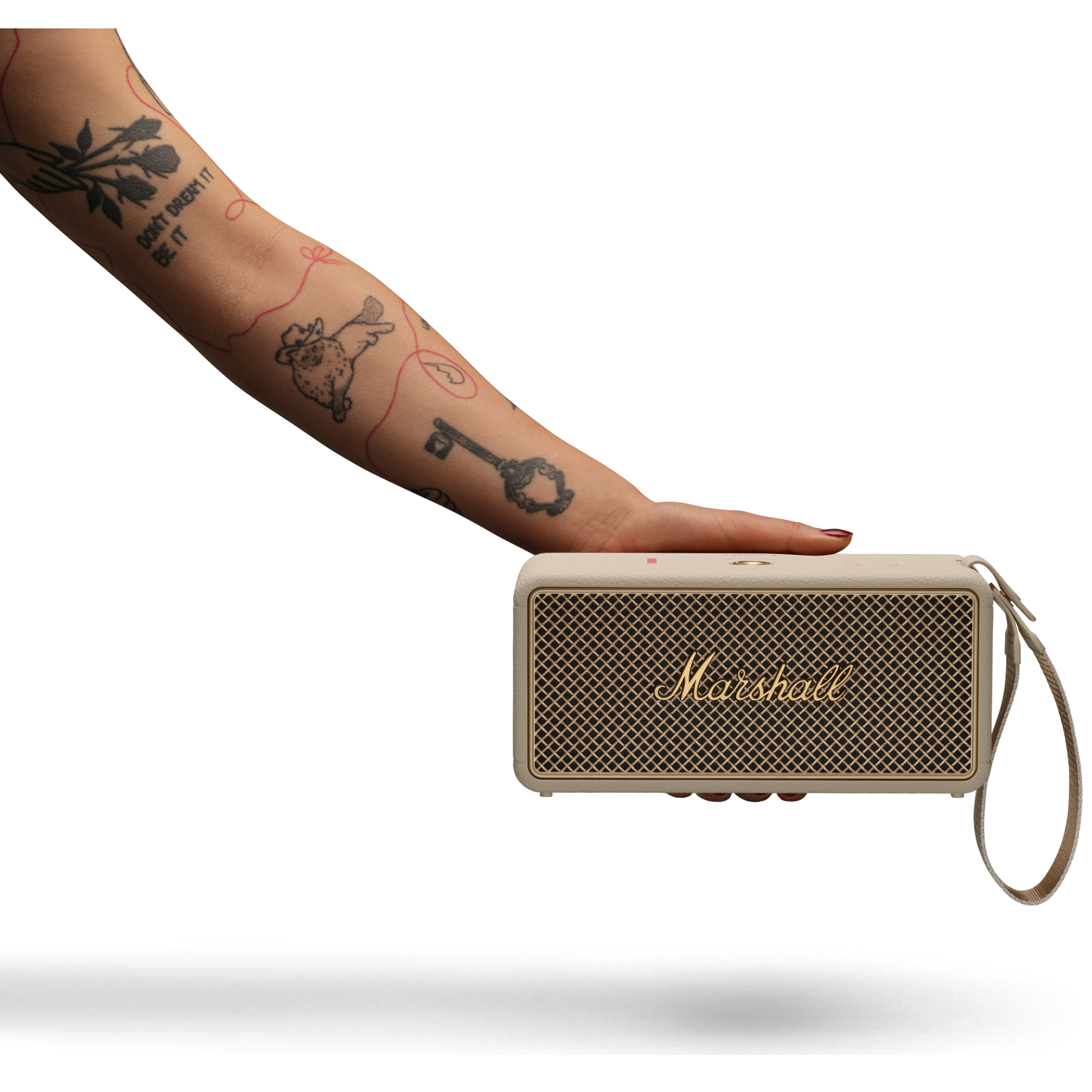 A tattooed arm holds a cream Marshall speaker with a gold grille. White background.