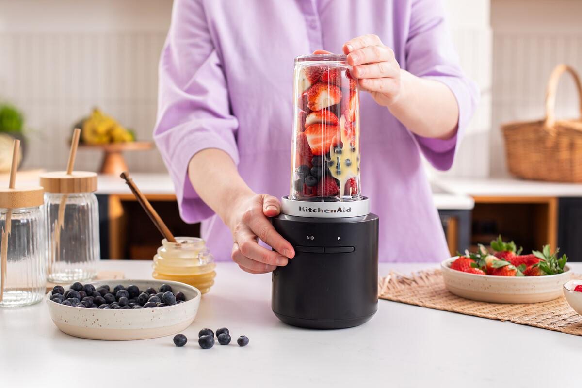 Person bereitet Obst-Smoothie im Mixer zu. Erdbeeren, Blaubeeren und Sahne.
