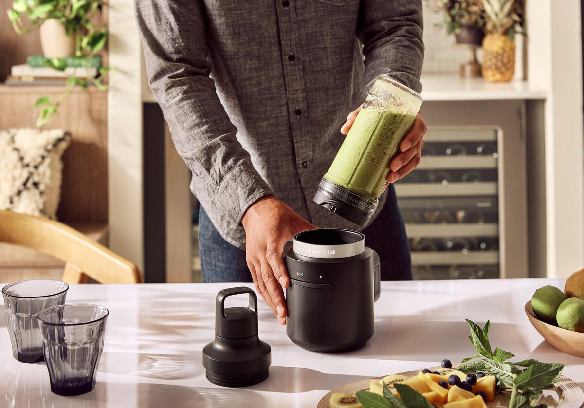 Mann hält Mixerbehälter mit Smoothie über schwarzes Mixergehäuse.