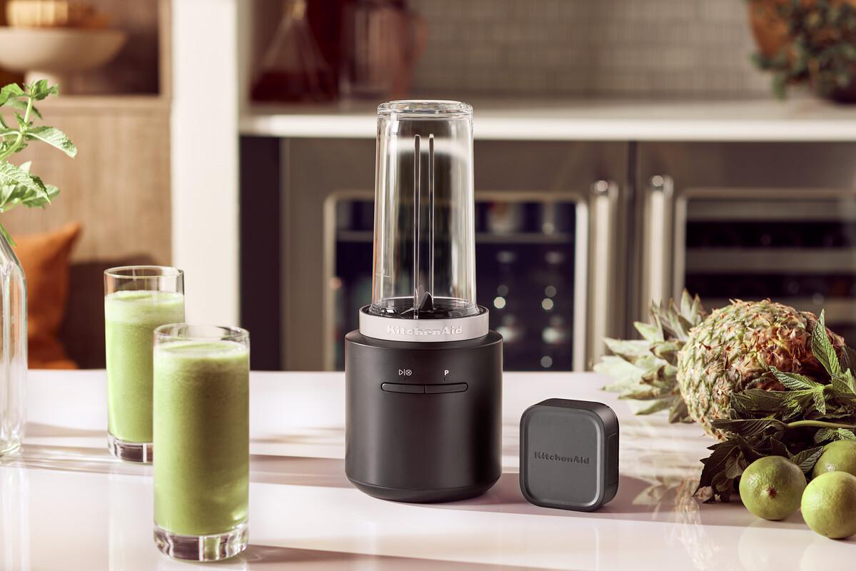 Ein schwarzer Mixer mit einem Glas Behälter, zwei Gläsern Smoothie, einer Ananas und Limetten.