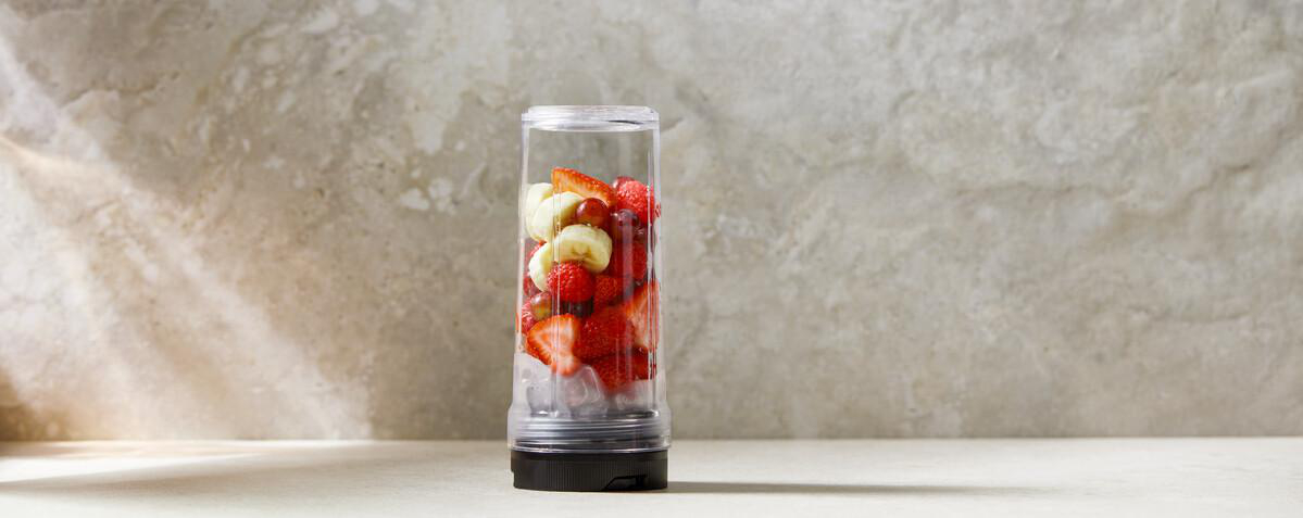 Ein durchsichtiger Behälter mit Erdbeeren, Bananen und Trauben auf Eiswürfeln.
