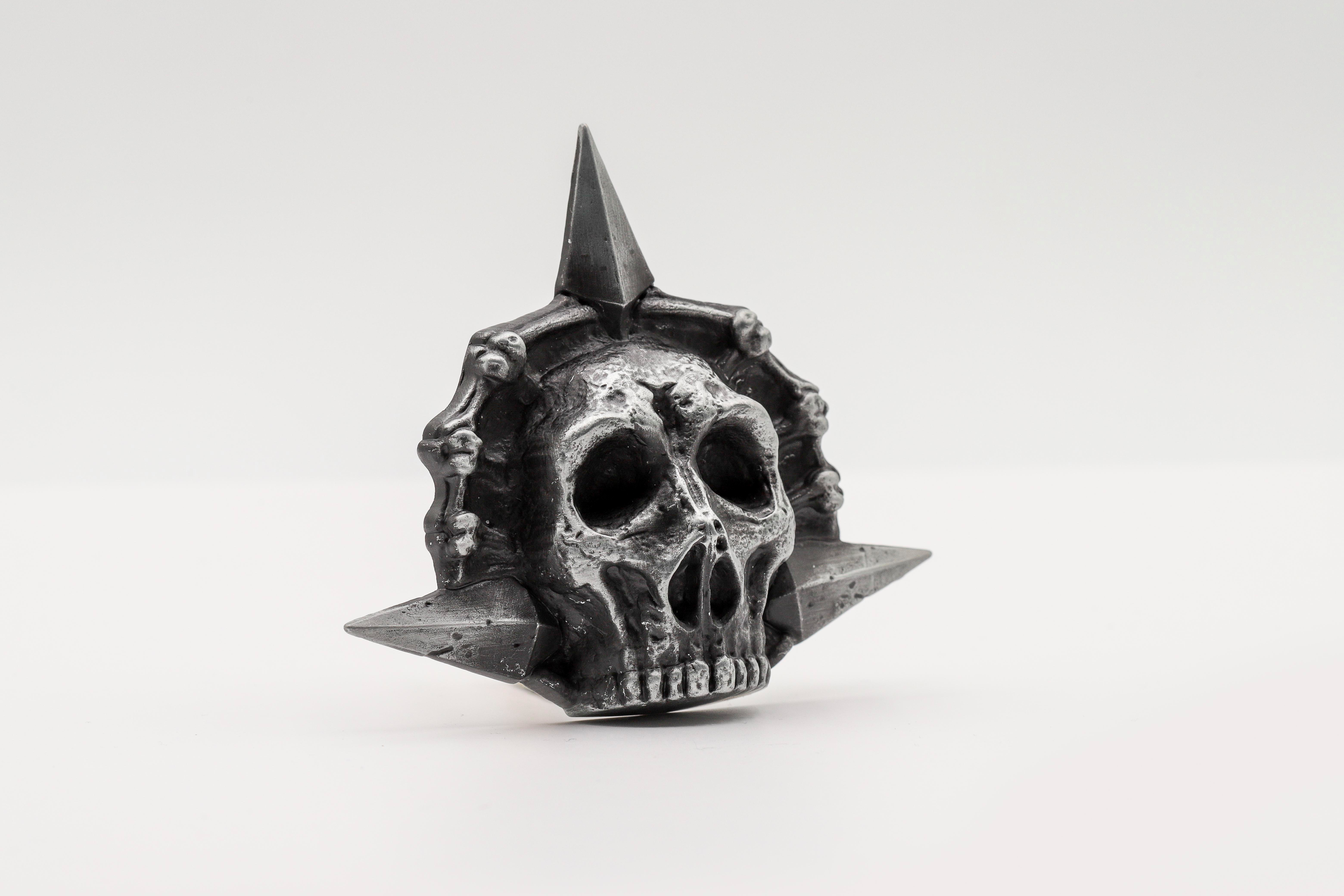 Ein silbernes Totenkopf-Symbol mit spitzen Zacken und Schädeln.