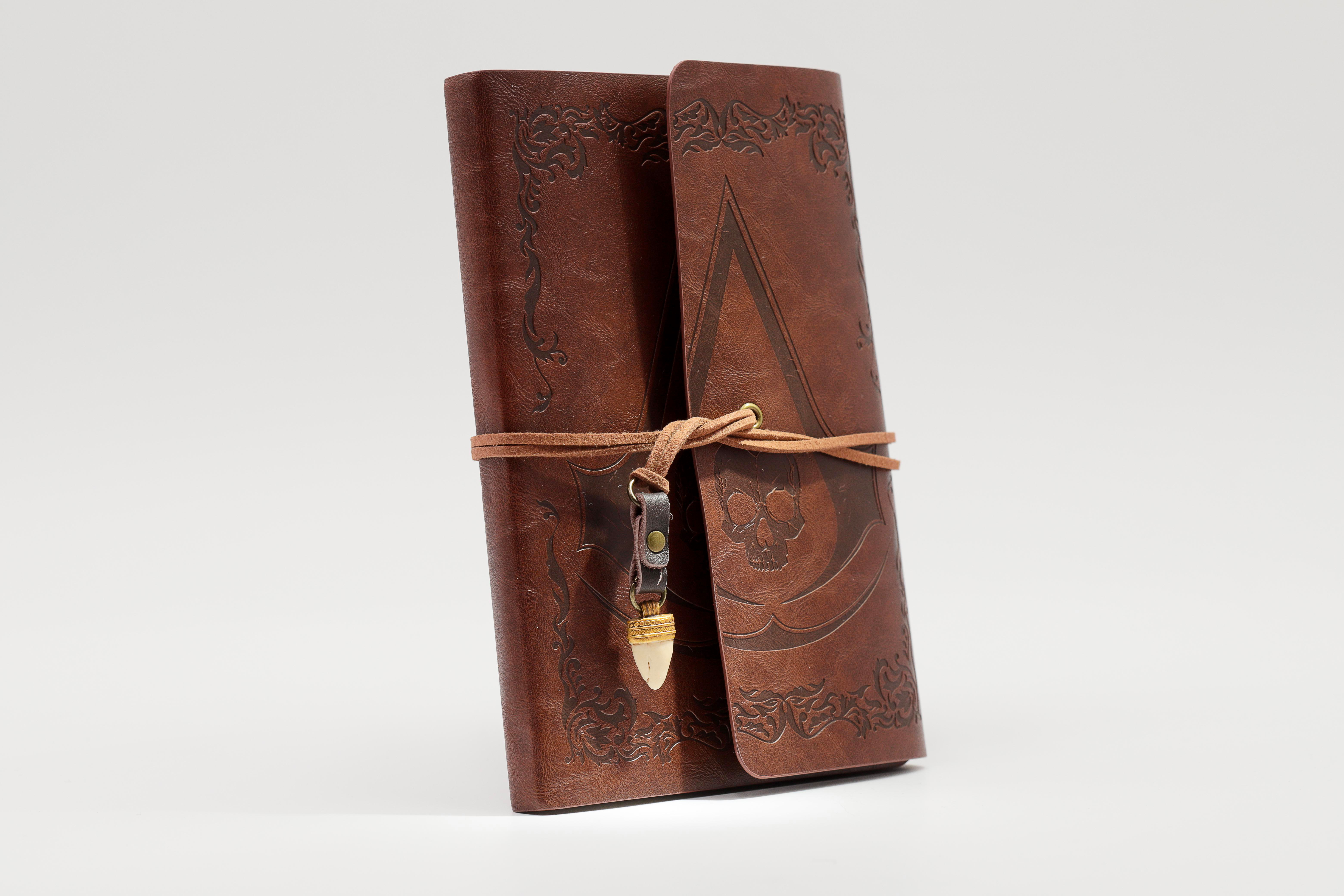 Ein braunes Lederbuch mit Schnalle und Totenkopfprägung, auf weißem Hintergrund.