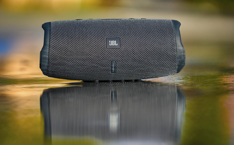 Ein grauer JBL Lautsprecher liegt auf einer nassen Oberfläche, mit Spiegelung.