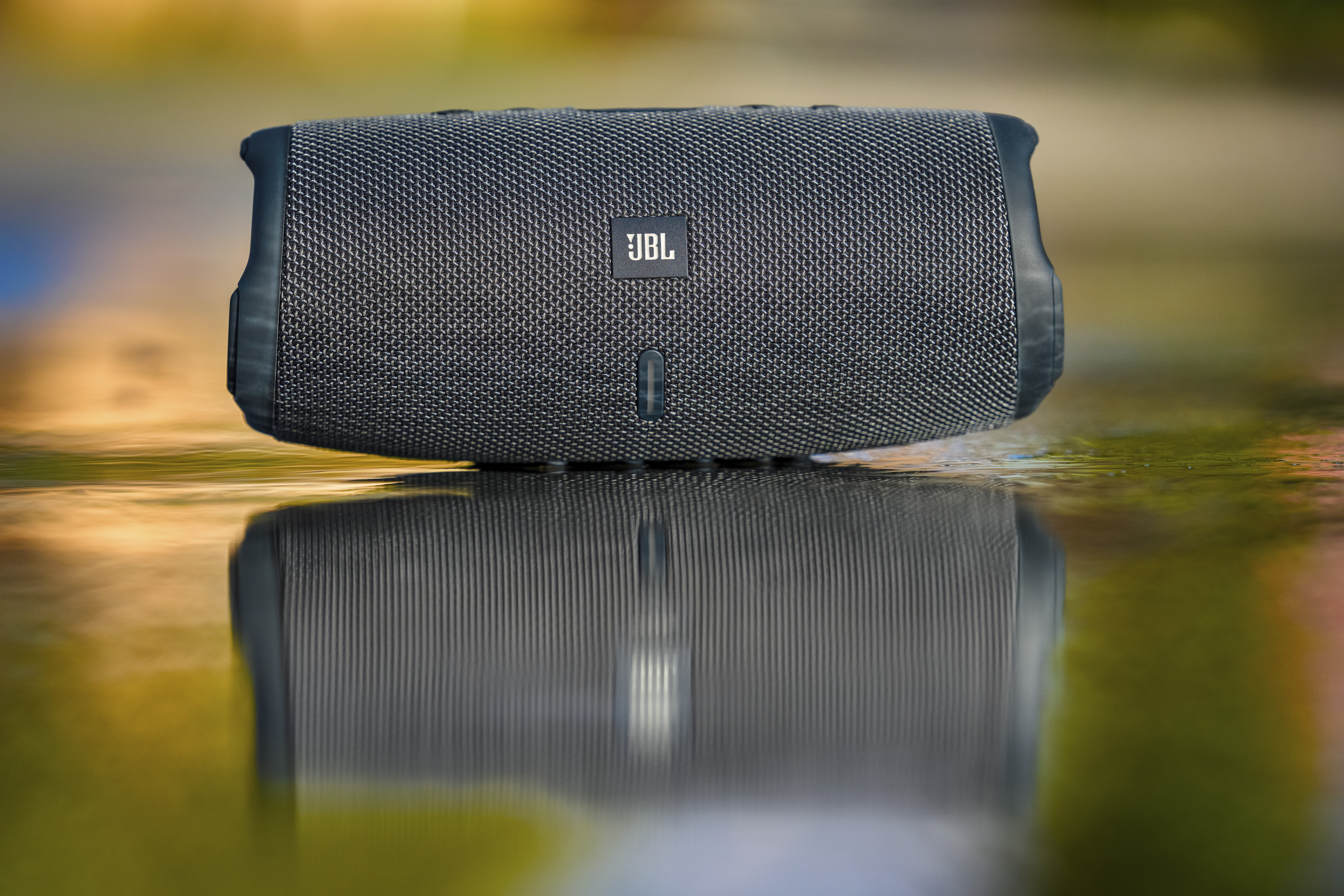 Ein schwarzer JBL Bluetooth-Lautsprecher ruht auf einer nassen Oberfläche, mit Spiegelung.