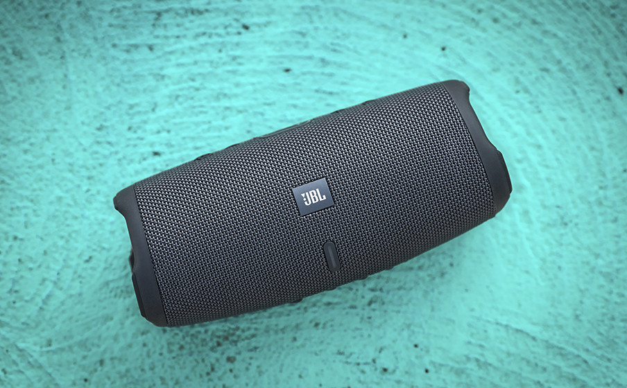 Ein schwarzer JBL Bluetooth-Lautsprecher liegt auf einem türkisfarbenen Untergrund.