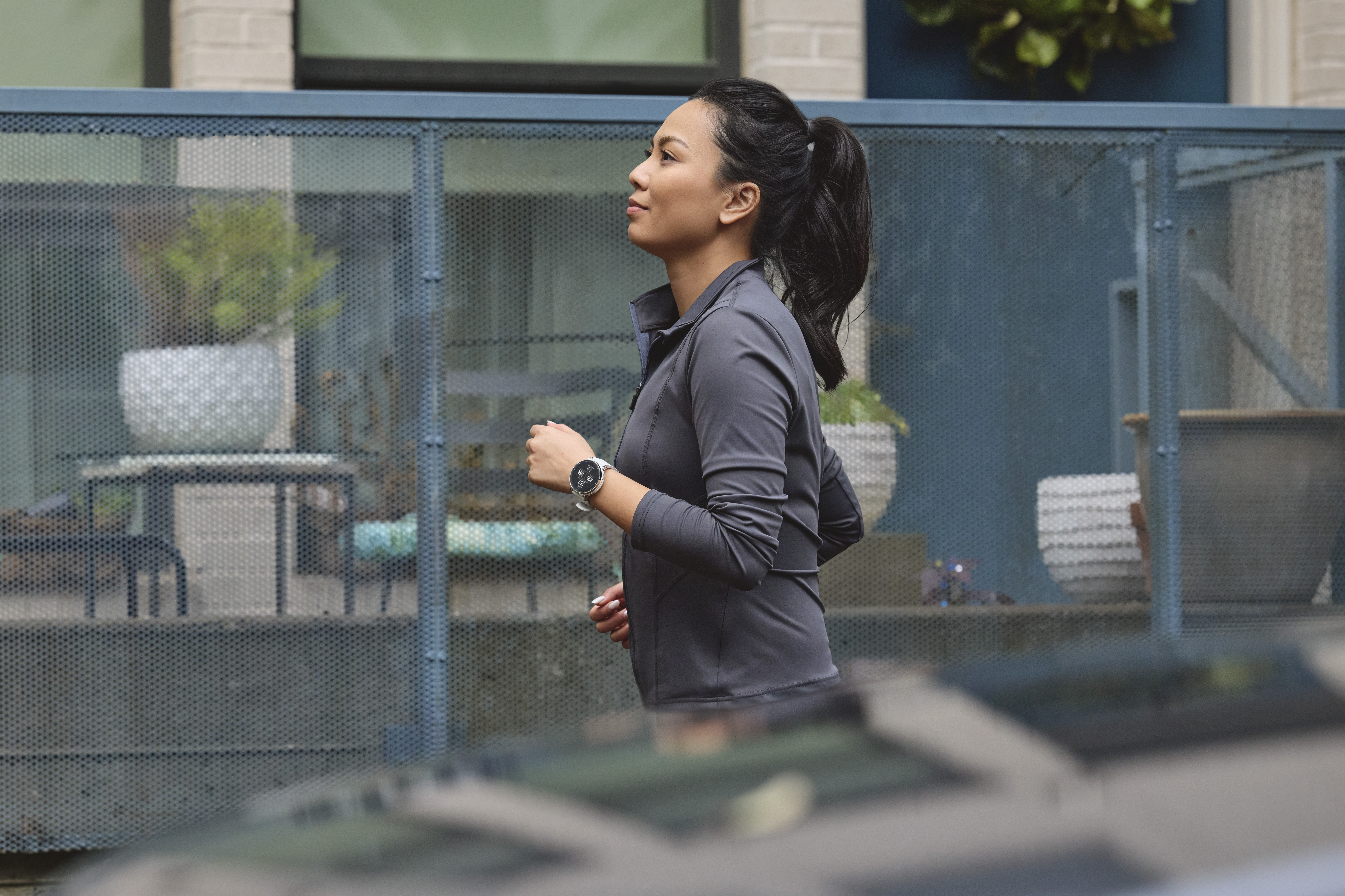 Une femme en haut de course gris court vers la droite, portant une montre de sport.