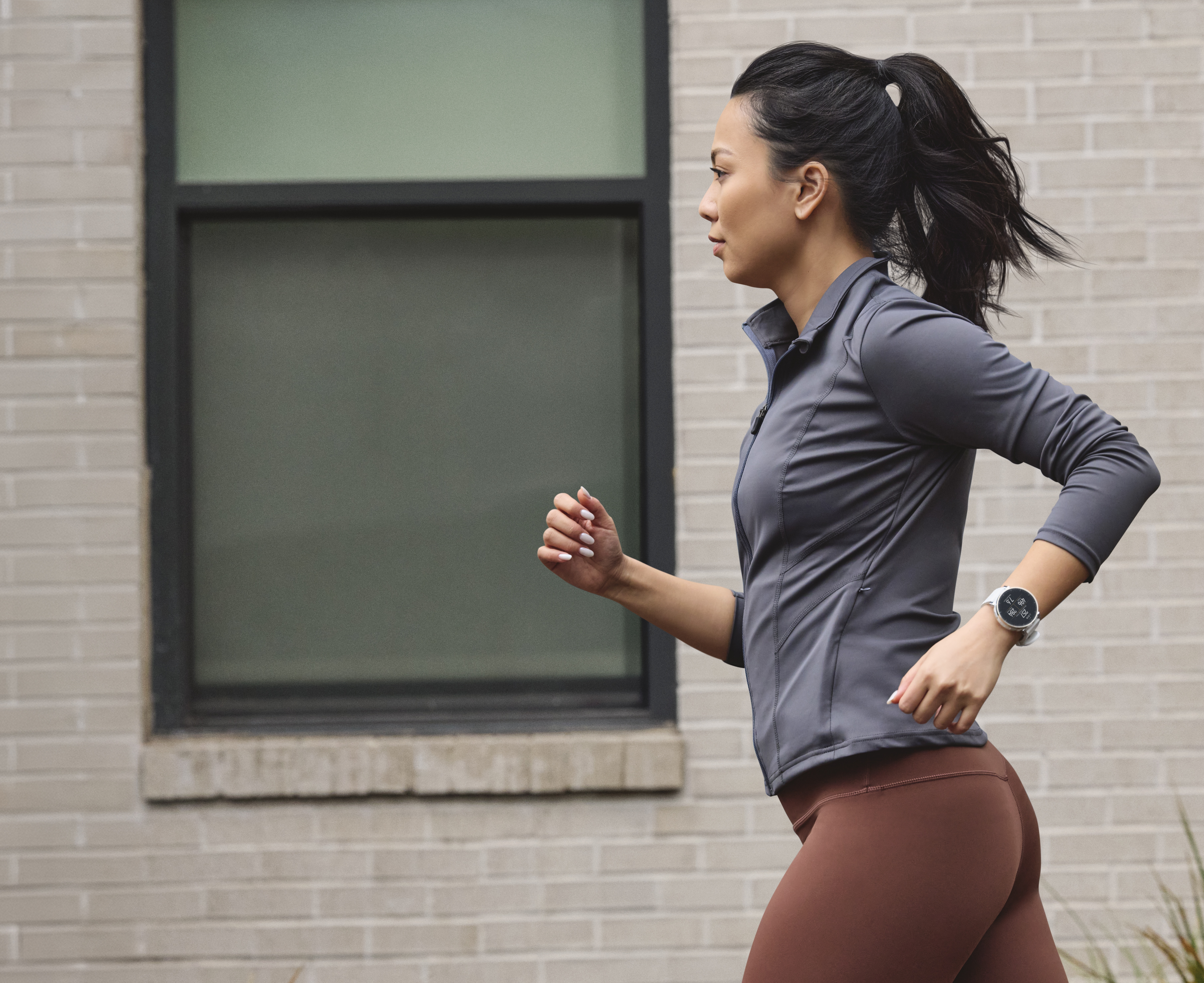 Une femme en tenue de sport court devant un mur de briques.