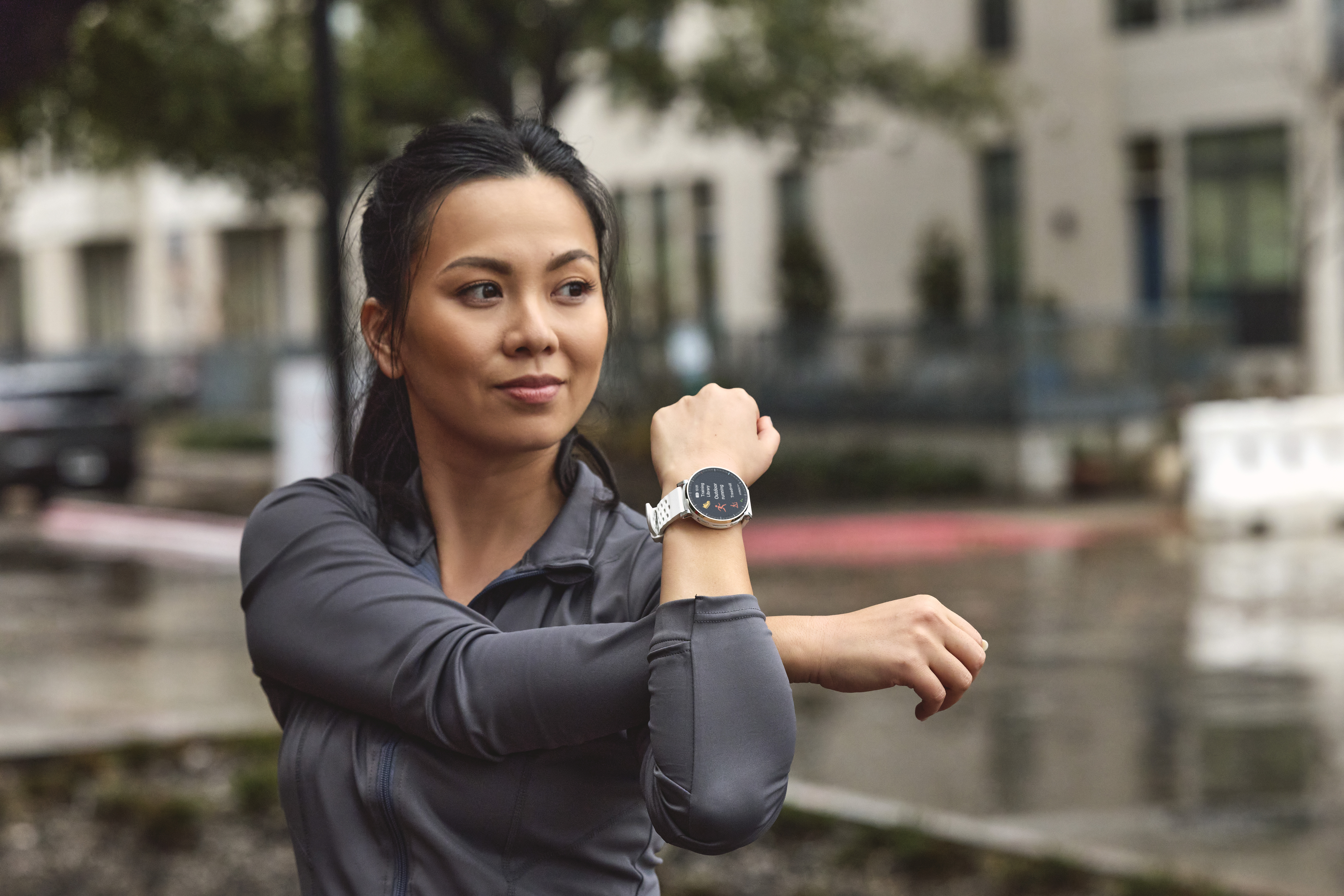 Une femme s'étire à l'extérieur, portant une montre connectée à son poignet.