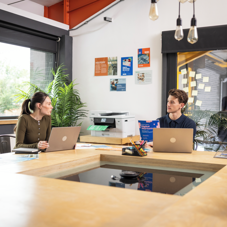Mężczyzna i kobieta przy biurku z laptopami i drukarką w biurze.
