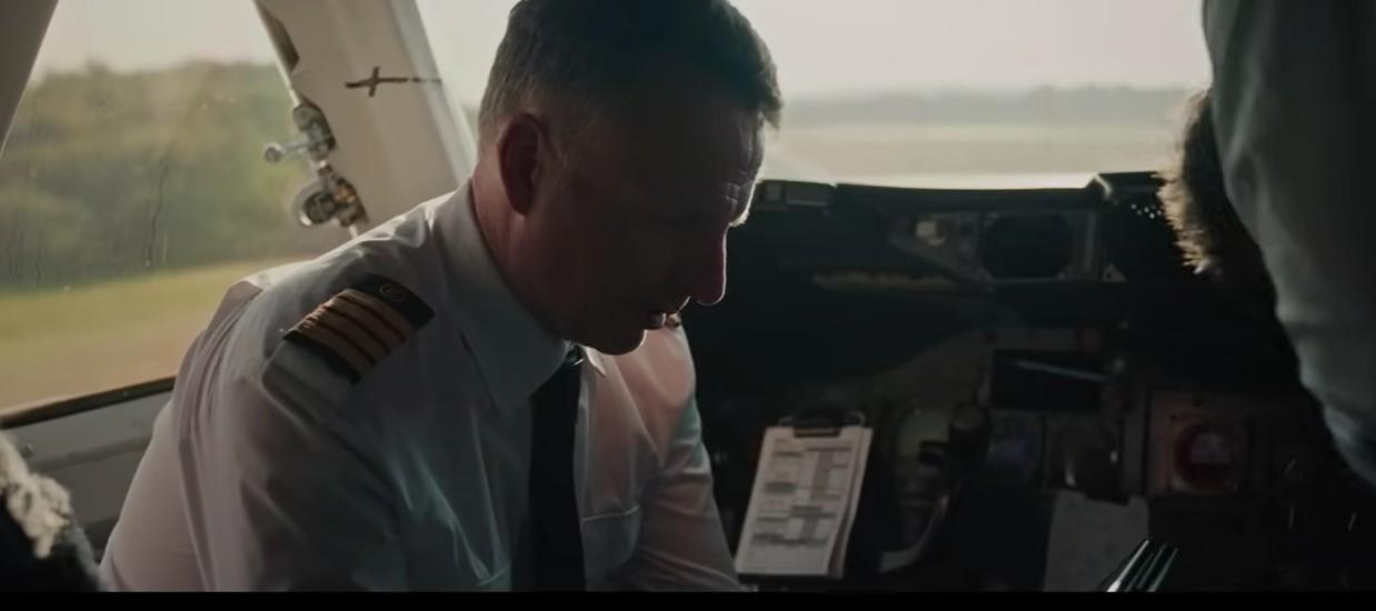 Pilot in Uniform blickt nach unten auf ein Klemmbrett im Cockpit.