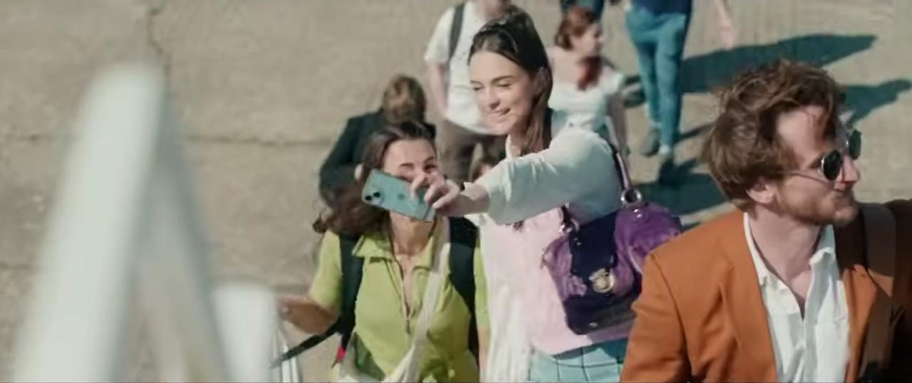 Eine Frau macht ein Selfie mit einem Handy, umgeben von anderen Menschen auf einer Treppe.
