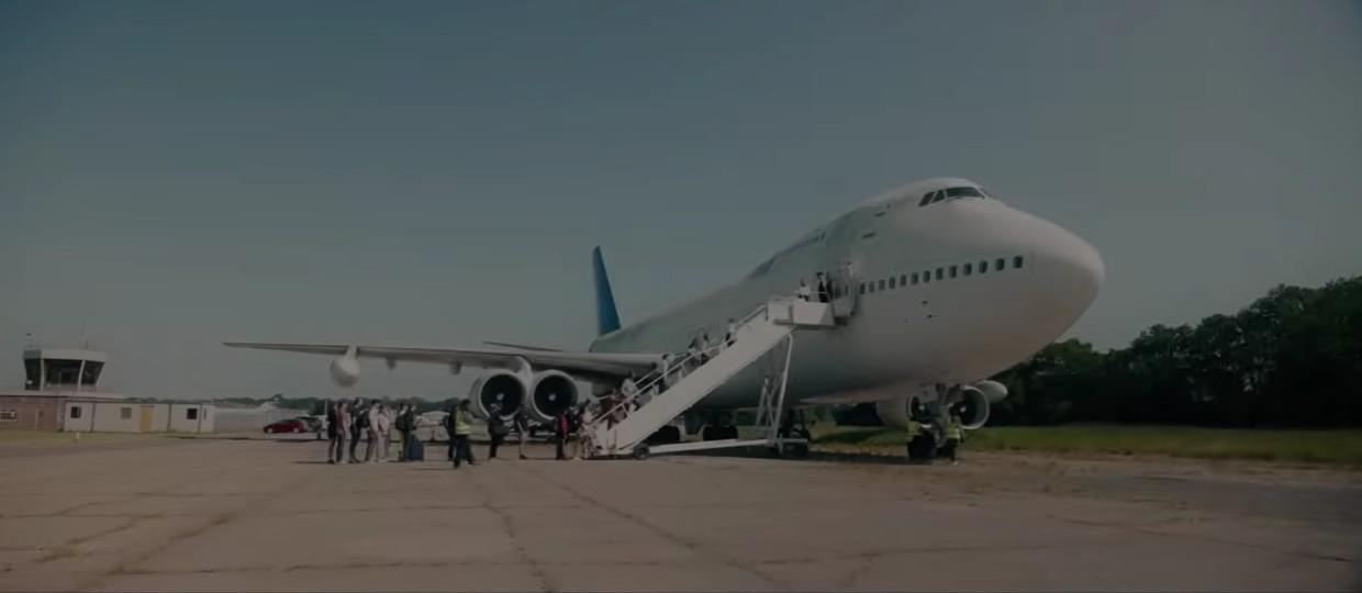 Ein großes weißes Flugzeug mit einer Treppe, auf der Menschen einsteigen. Ein Kontrollturm ist im Hintergrund.