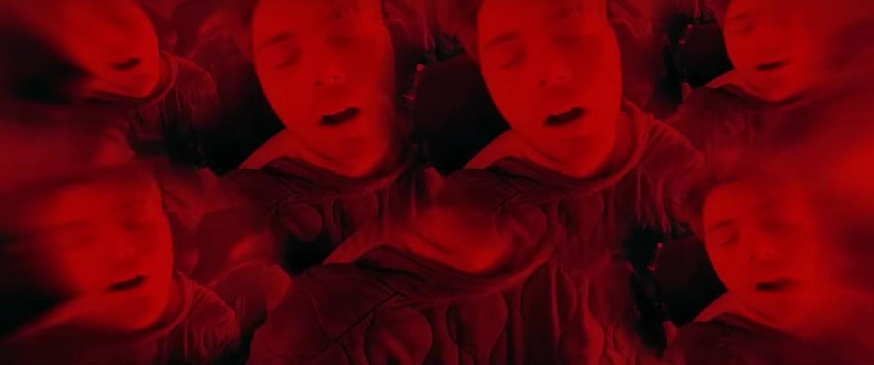 Viele Personen mit geschlossenen Augen, rot gefärbt, mit verzerrten Gesichtern.