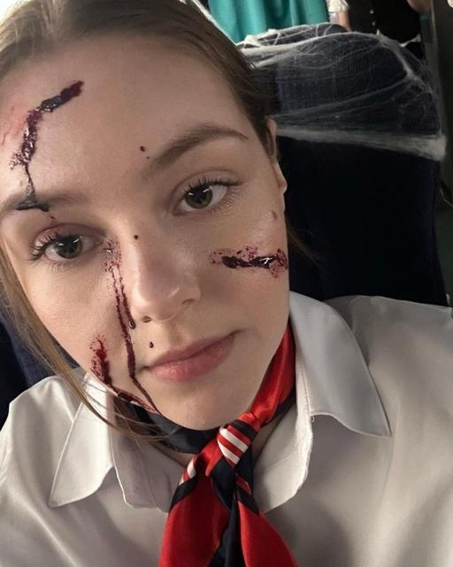 Junge Frau mit Kunstblut im Gesicht, weißem Hemd und rot/blauem Schal.