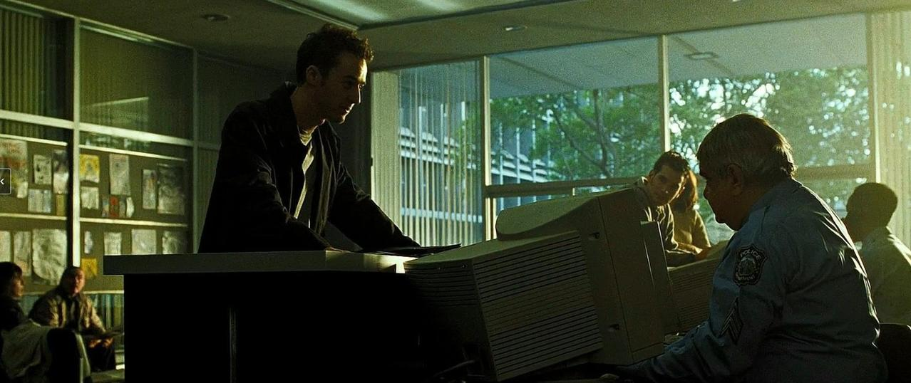Männer in einem schwach beleuchteten Büro mit einem großen Monitor und Papieren an der Wand.