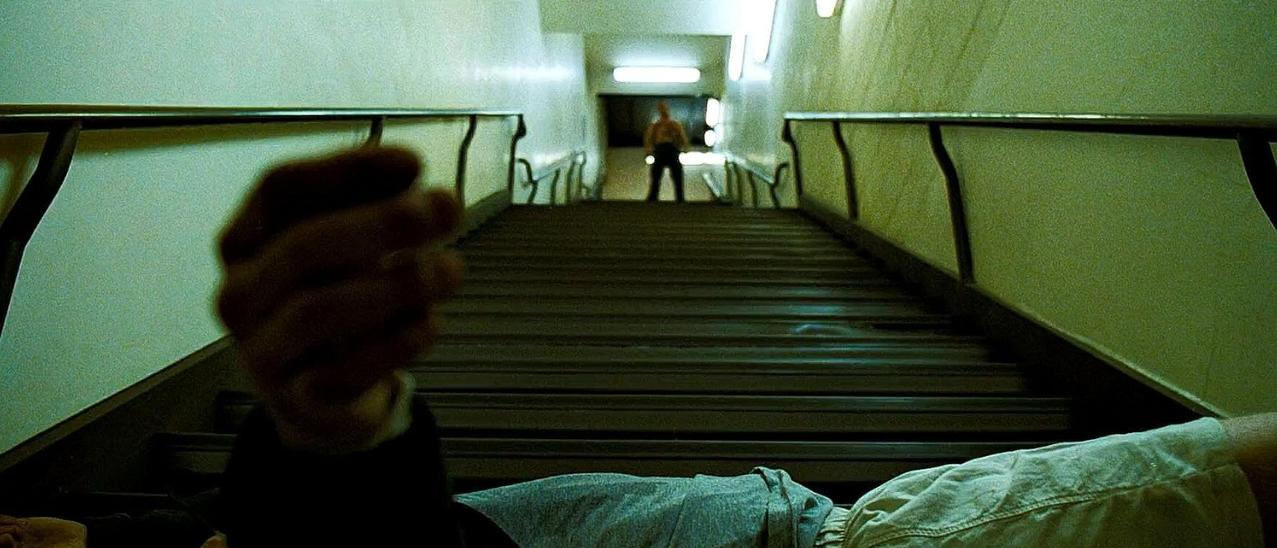 Eine Person liegt auf einer Treppe. Eine andere Person steht am oberen Ende.