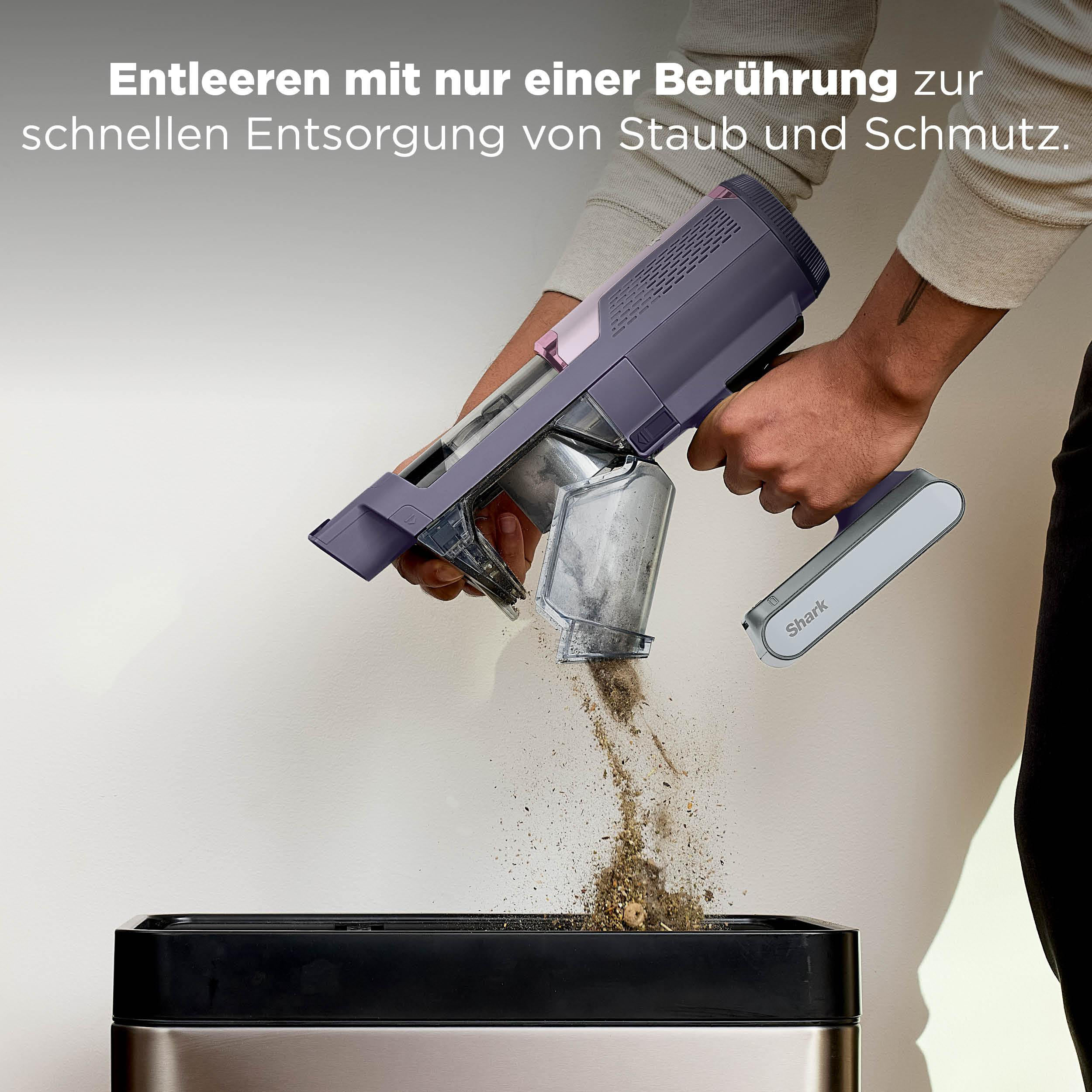 Eine Hand leert einen Handstaubsauger in einen Mülleimer. Staub fällt heraus.