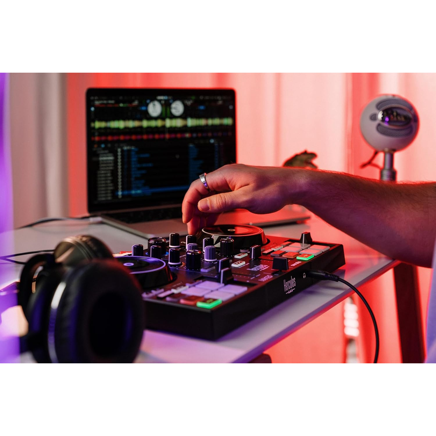 Controller DJ, laptop, cuffie e microfono su una scrivania con illuminazione rossa.