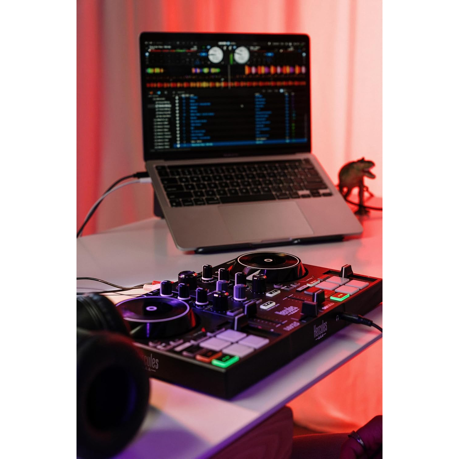 Un controller DJ e un laptop su un tavolo, illuminati da luce rossa.