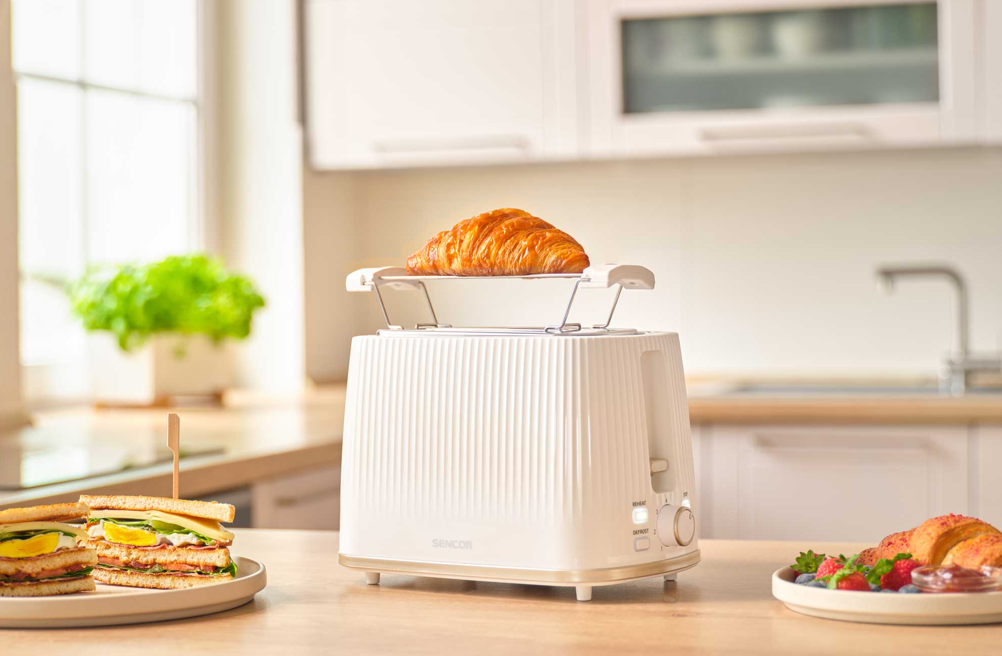 Fehér kenyérpirító croissanttal és szendvicsekkel fa asztalon.