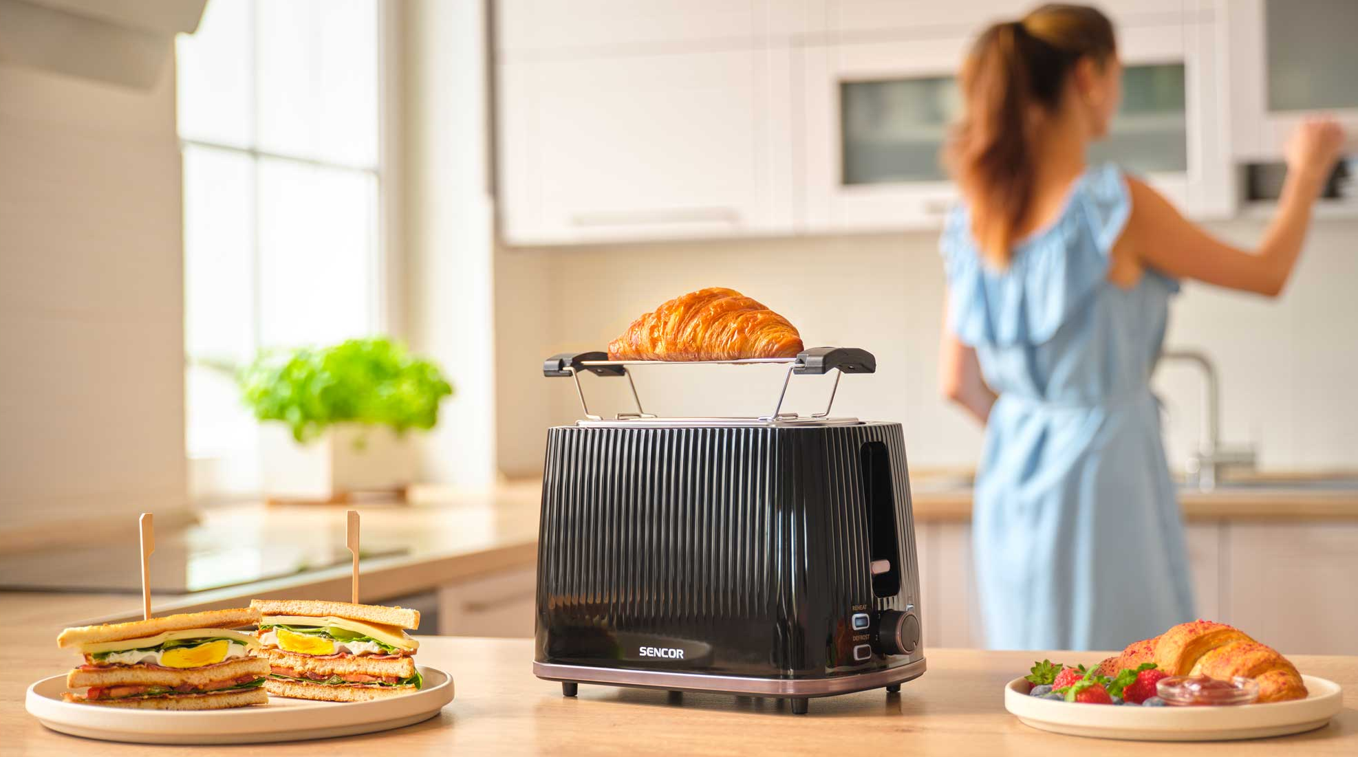 Fekete kenyérpirító croissanttal, szendvicsekkel és bogyós gyümölcsökkel fa asztalon.
