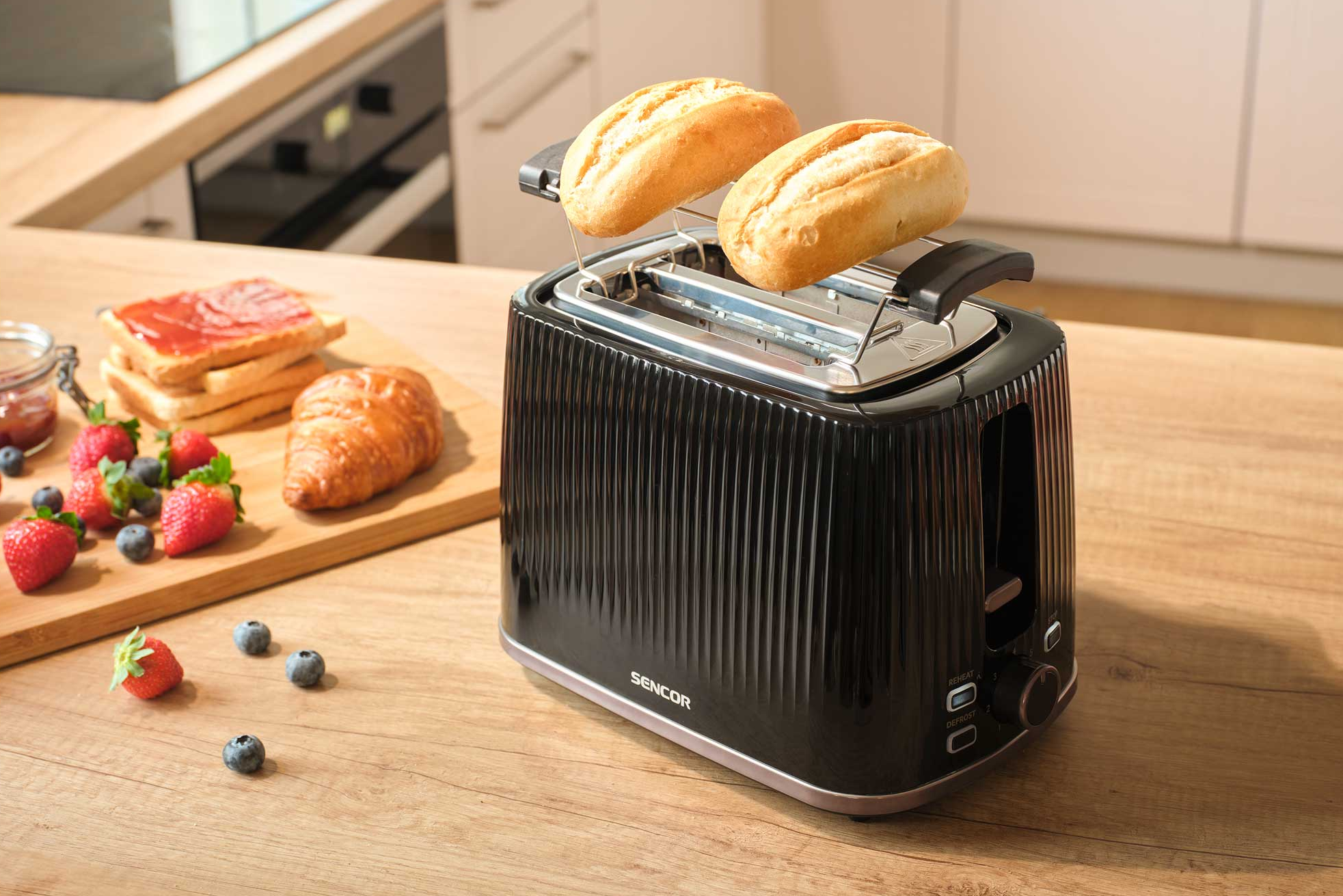 Fekete kenyérpirító két zsömlével, mellette pirítós, croissant és bogyók.