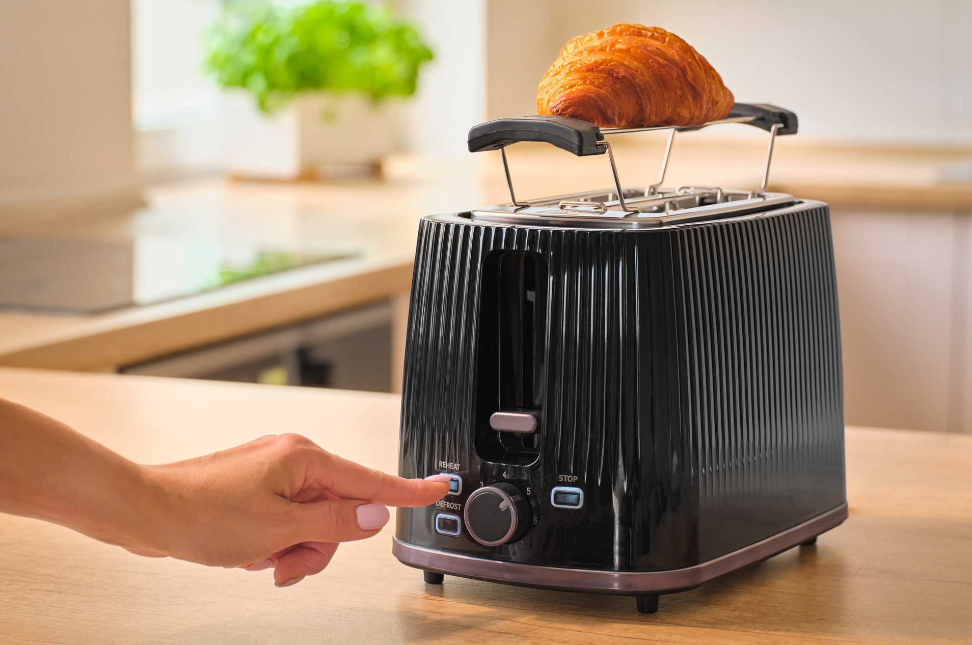 Egy kéz egy fekete kenyérpirítóra nyom, tetején croissanttal.