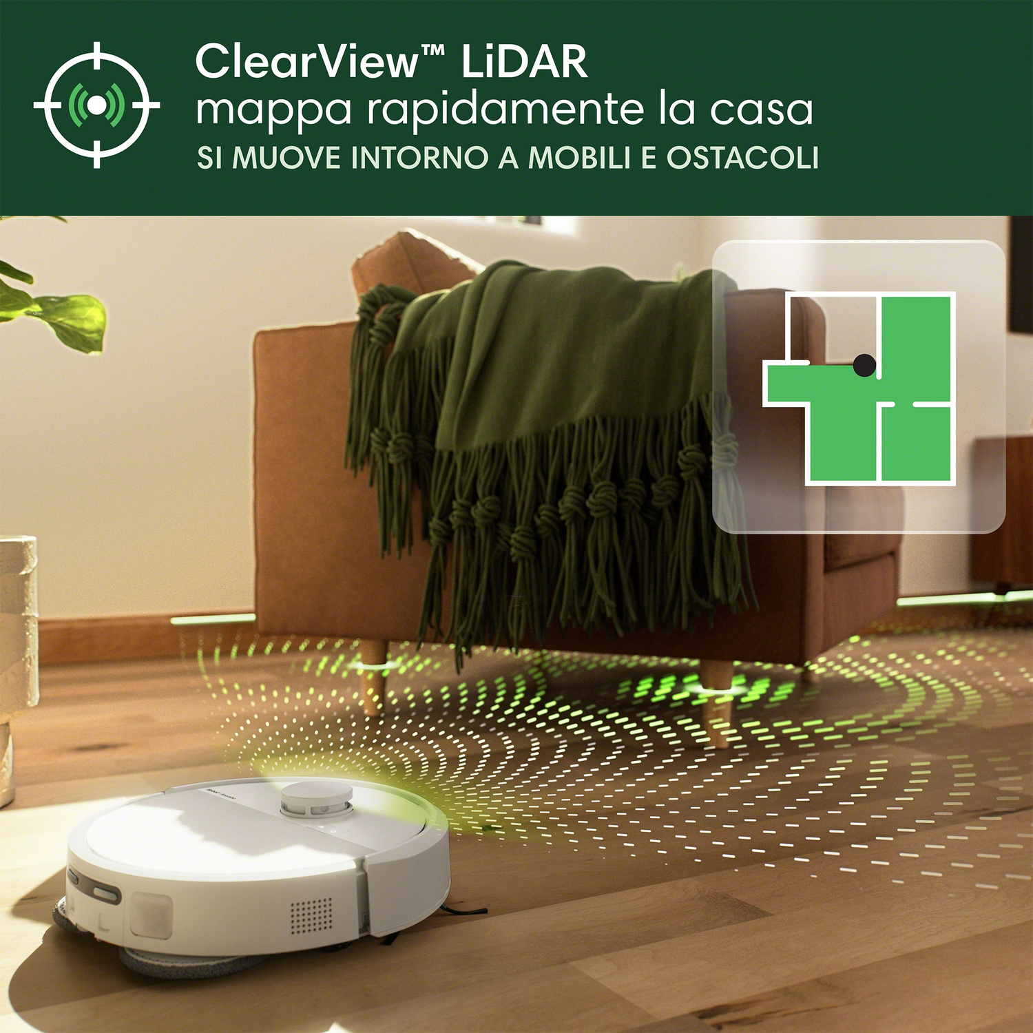 Un robot aspirapolvere bianco pulisce un pavimento in legno vicino a un divano con coperta verde.