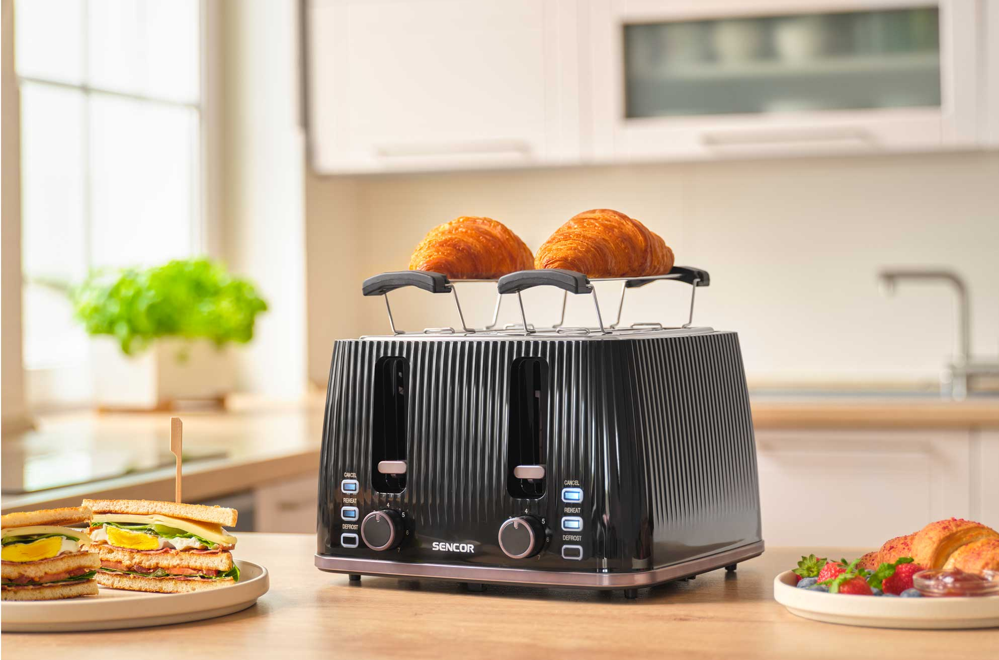 Fekete kenyérpirító két croissanttal, mellette szendviccsel és bogyókkal.