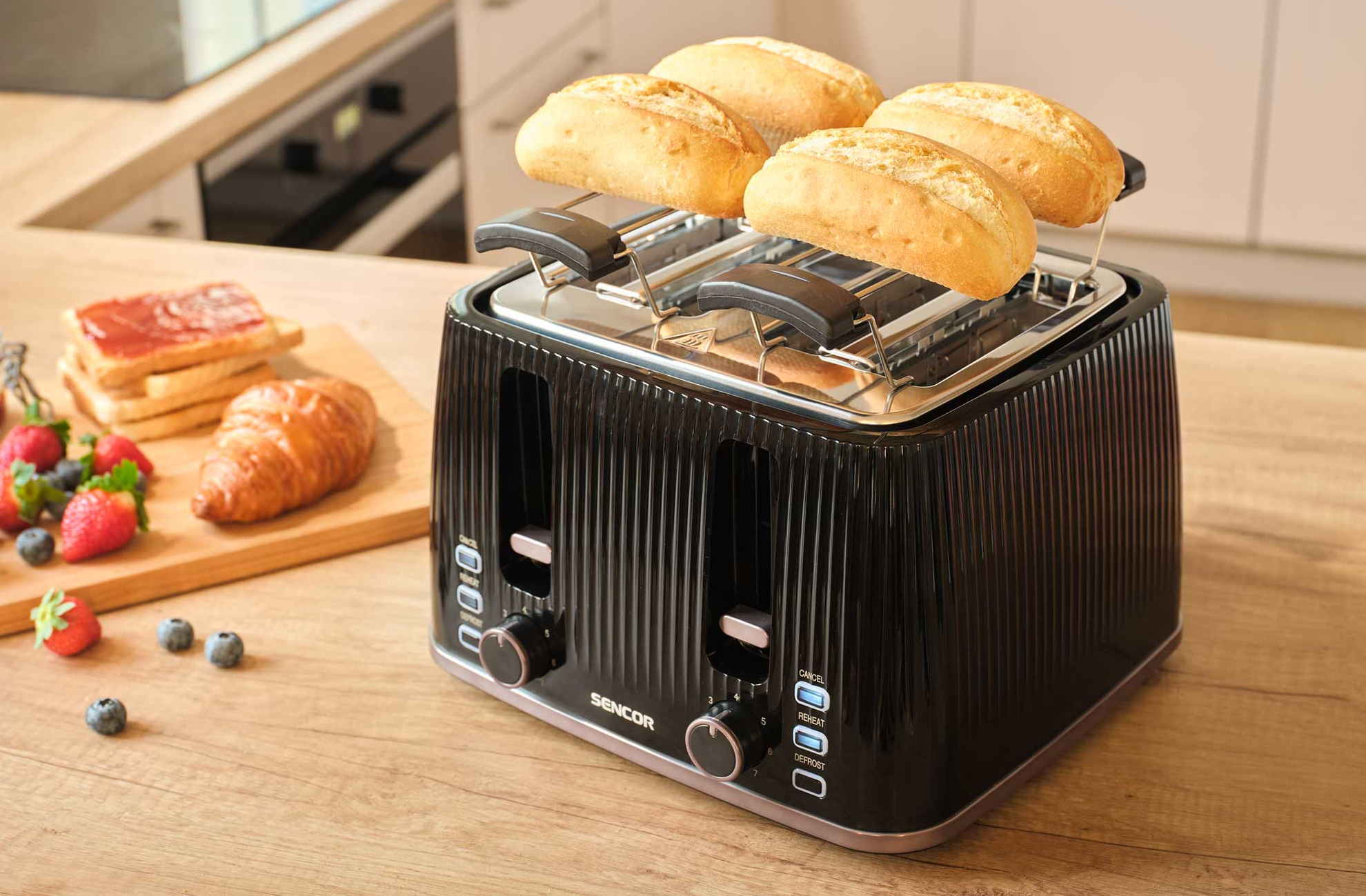 Fekete kenyérpirító négy zsemlével, pirítóssal, croissanttal és bogyókkal faasztalon.
