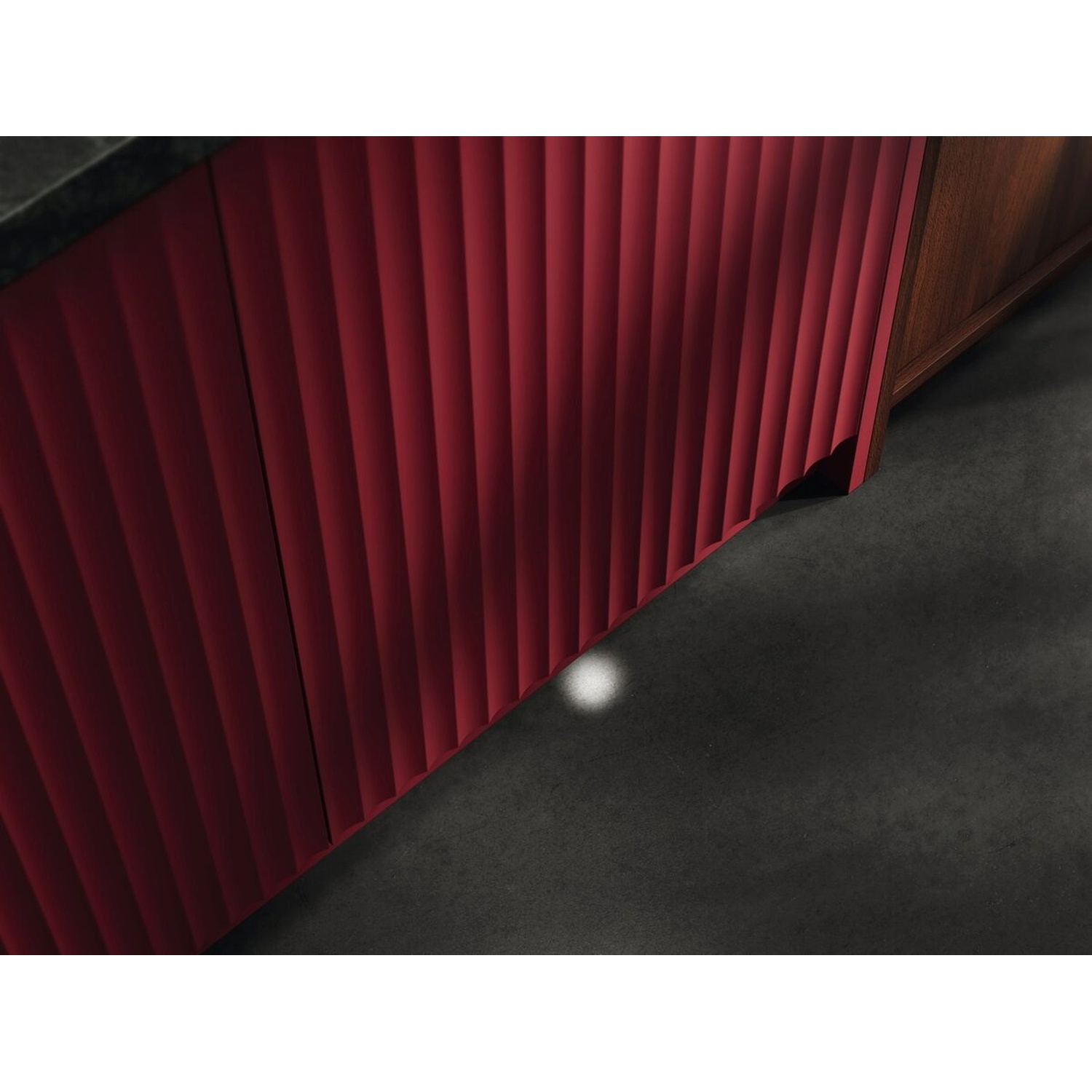 Frontale armadio rosso con scanalature verticali accanto a legno e pavimento scuro.