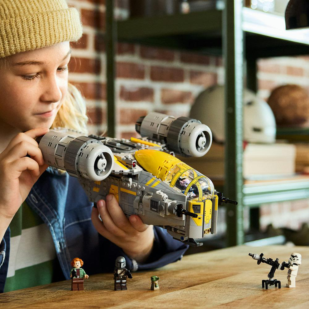 Kind hält LEGO-Raumschiff, Figuren und eine Kanone auf einem Holztisch.