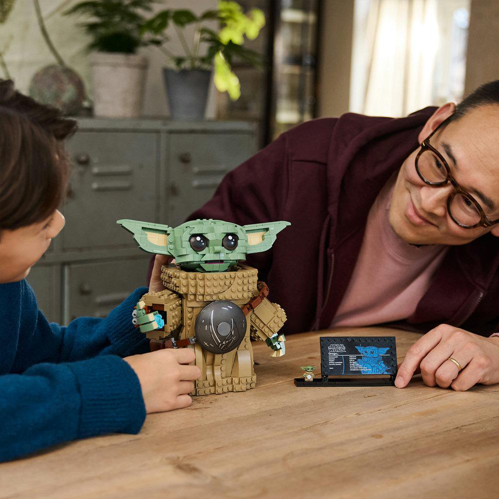 Ein Junge und ein Mann bauen eine Lego-Figur von Baby Yoda an einem Holztisch.