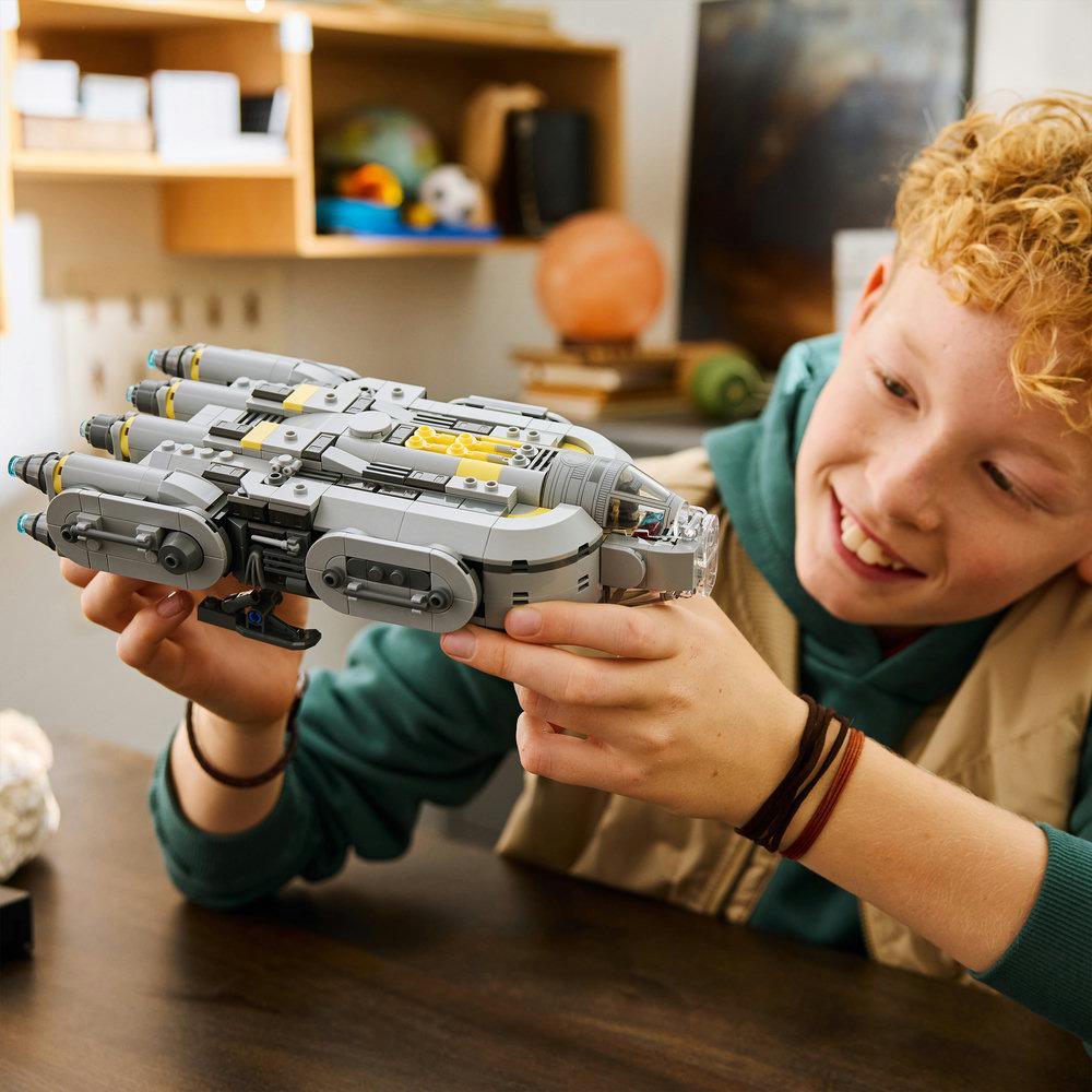 Ein Junge hält ein graues Lego-Raumschiff mit gelben Akzenten.
