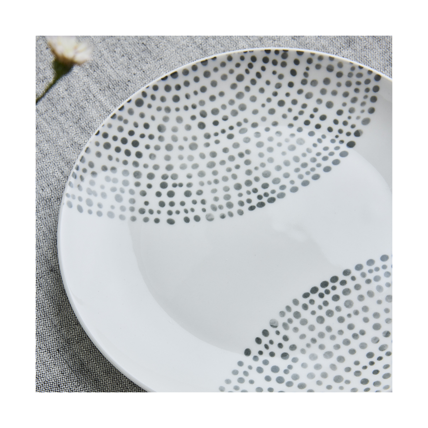 Piatto bianco con pois grigi, su tovaglia grigia con un fiore.